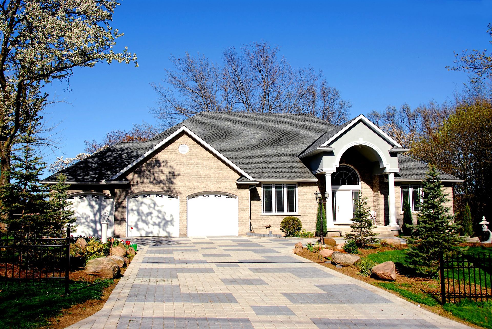 Single-story suburban house with stone facade, garage, and paved driveway under a blue sky
