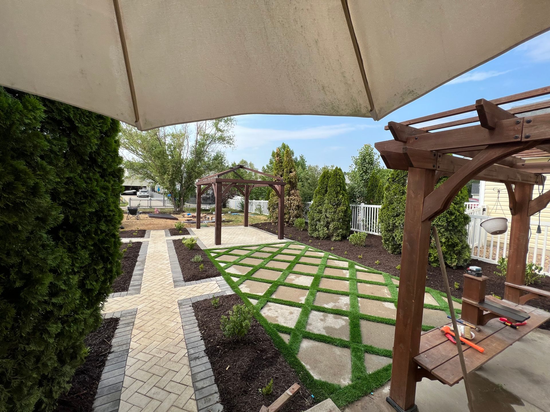 Backyard with stone pathway, pergola, and green, square artificial grass.