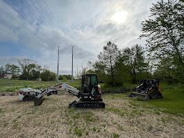 Three construction vehicles on grassy land with trees and utility poles in the background.