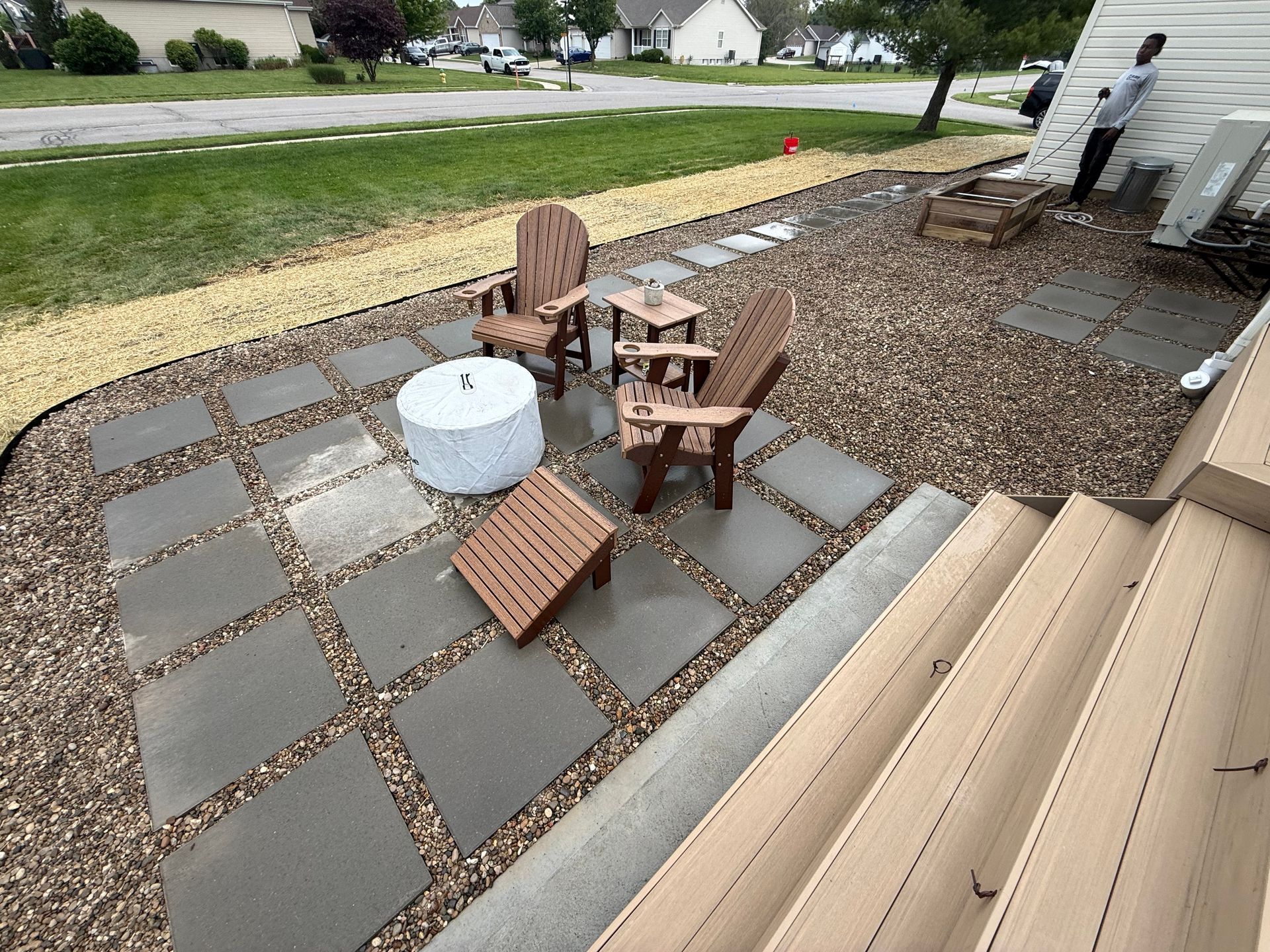 Back patio with stone pavers, chairs, and a white fire pit beside a gravel yard and lawn
