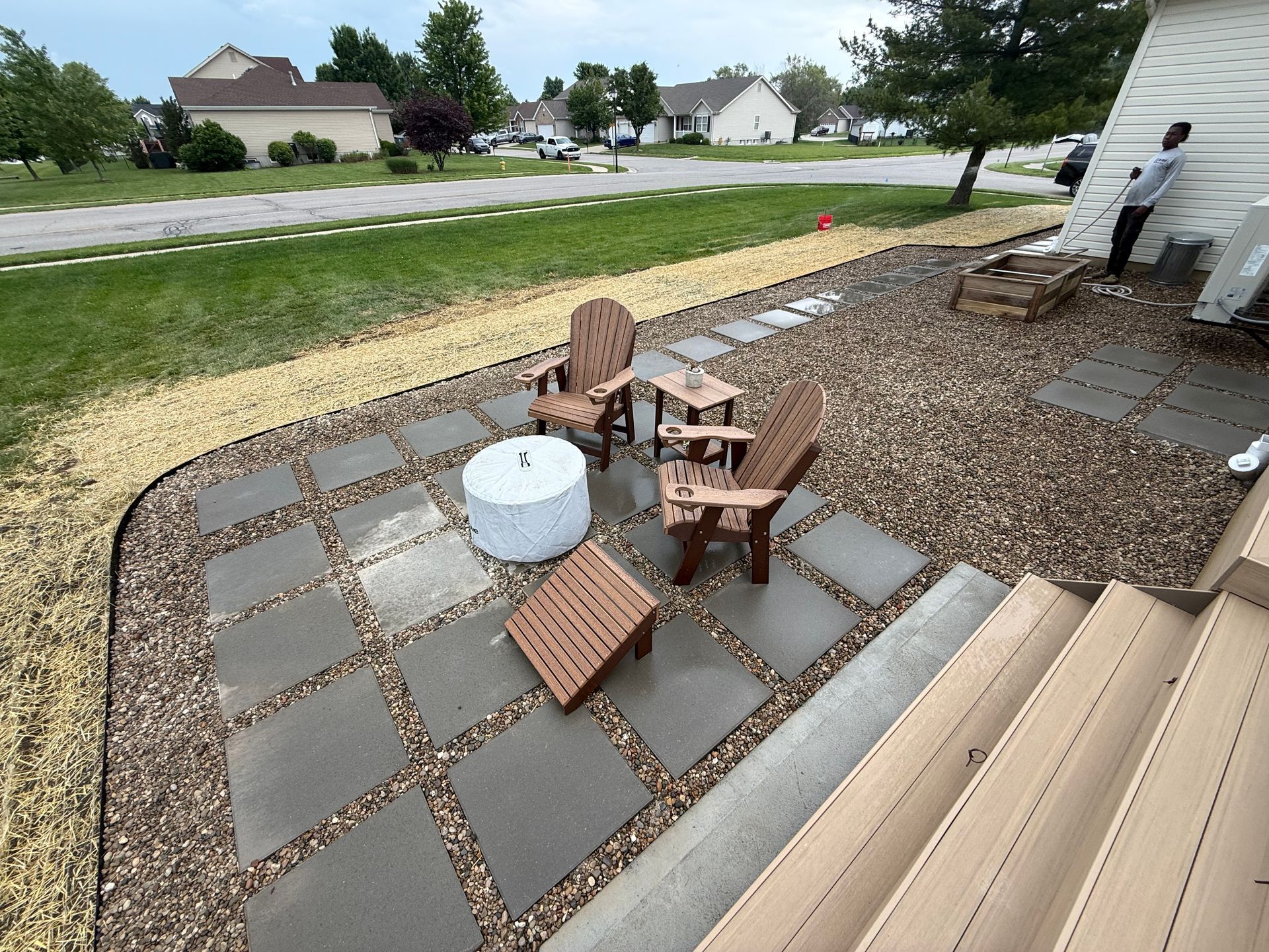 Backyard patio with paver seating area, wooden chairs, and a white fire pit beside a house.