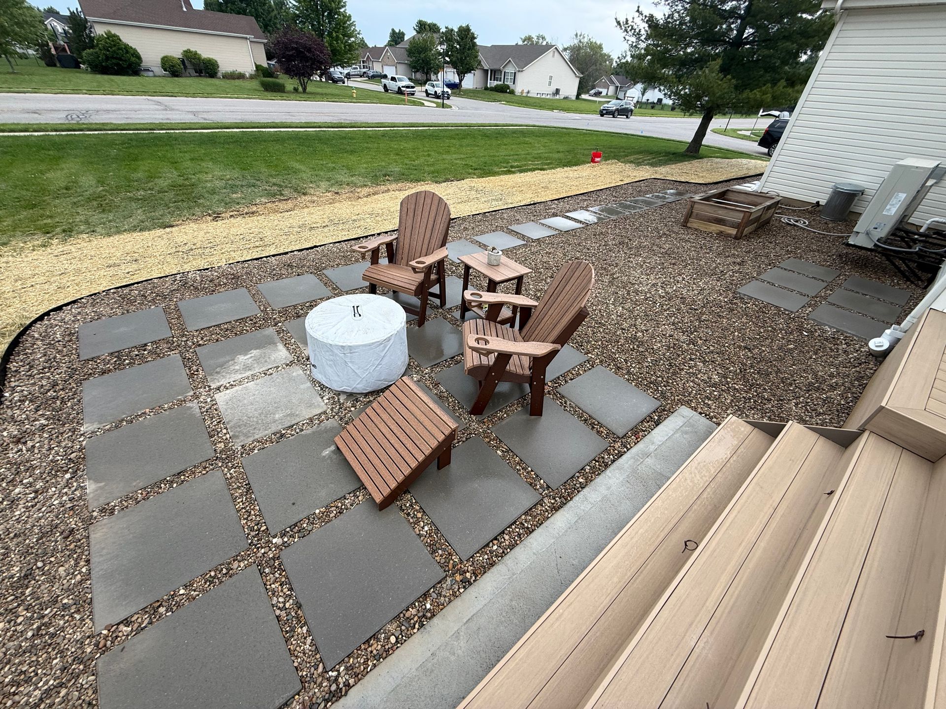 Backyard patio with pavers, two chairs, a small table, and a white planter near a house and lawn