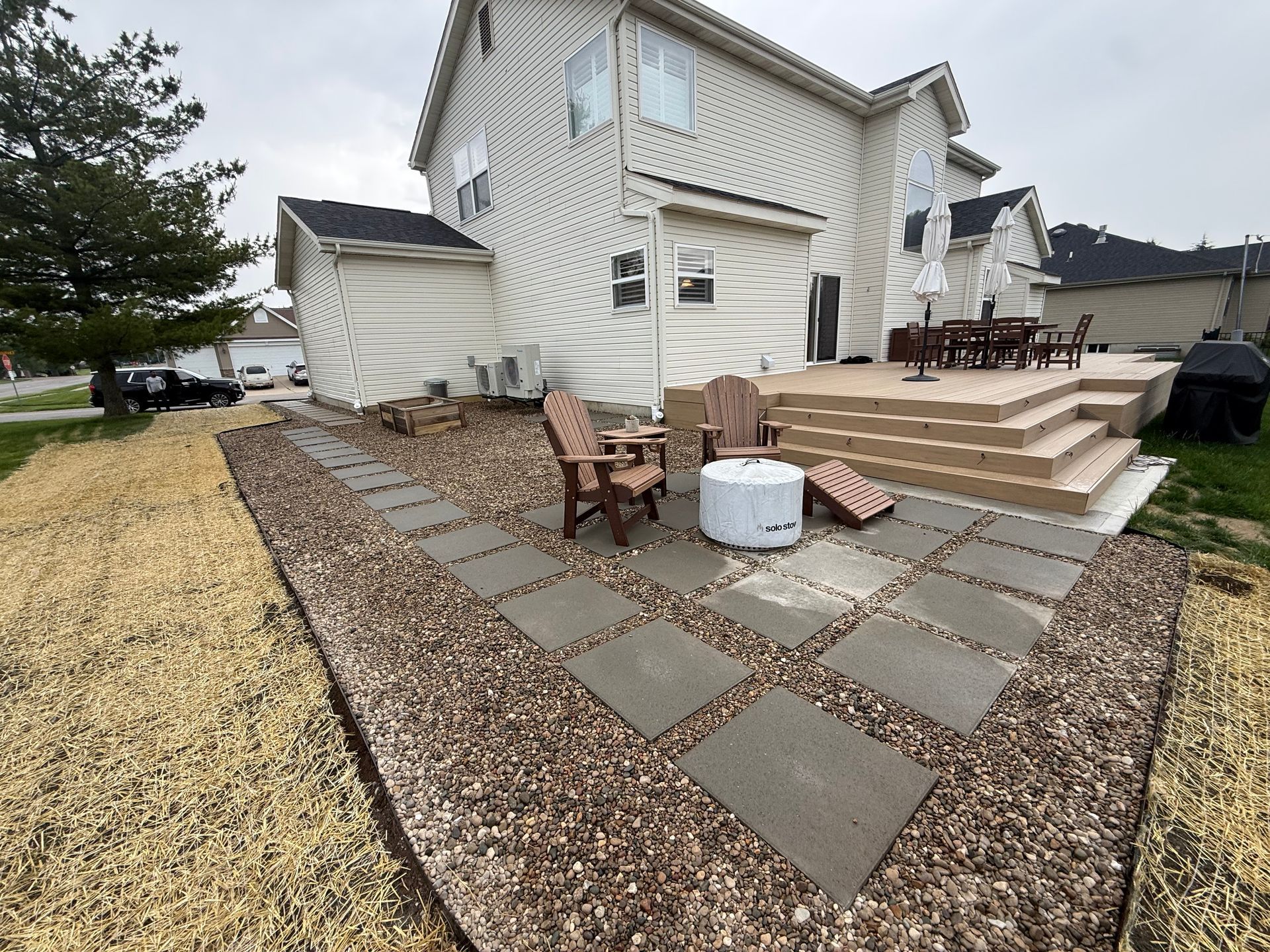 Backyard patio with fire pit, chairs, stone walkway, and a beige house after storm damage