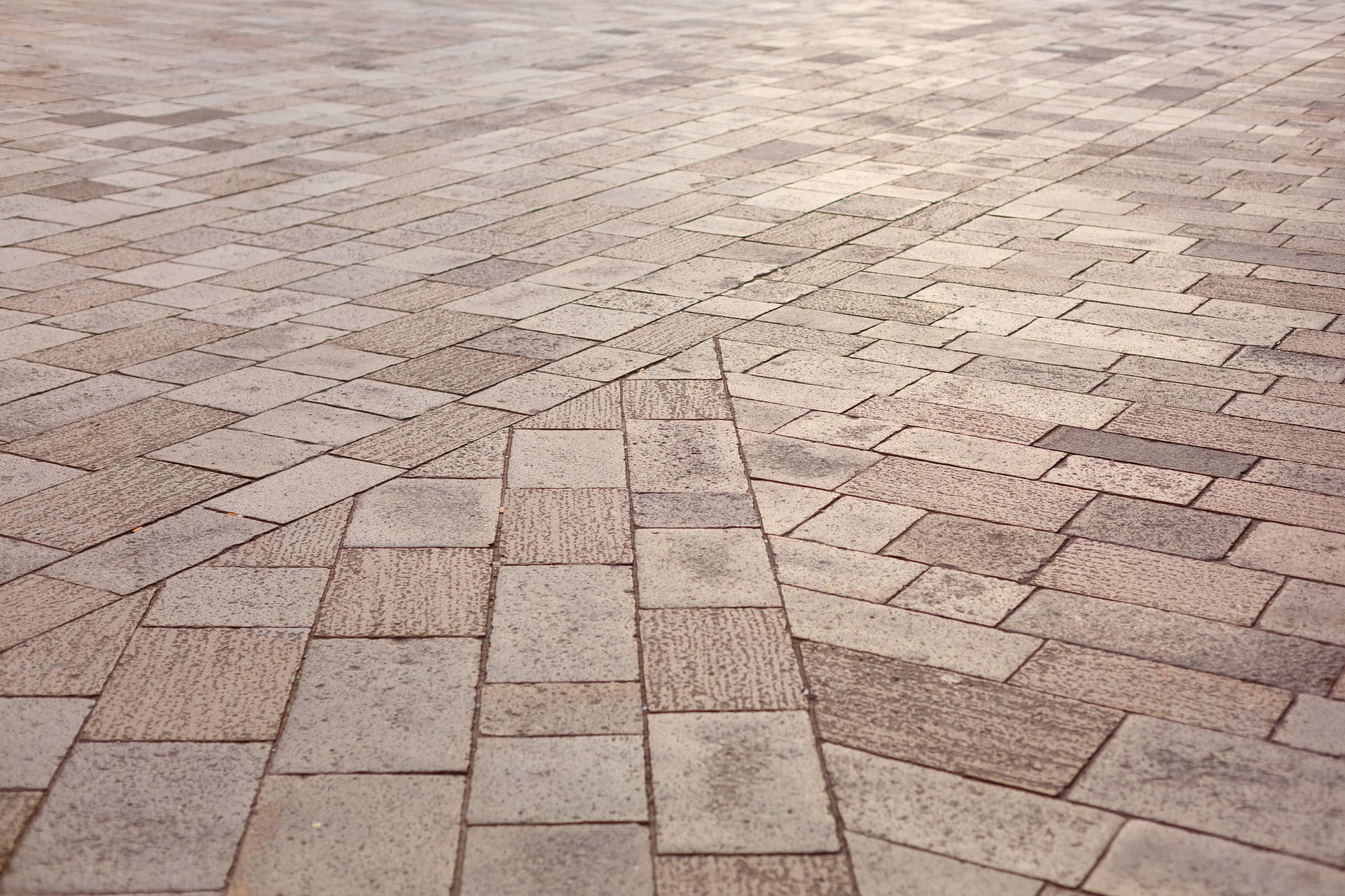 A ground-level view of light-colored, textured paving stones arranged in a geometric, multi-directional pattern.