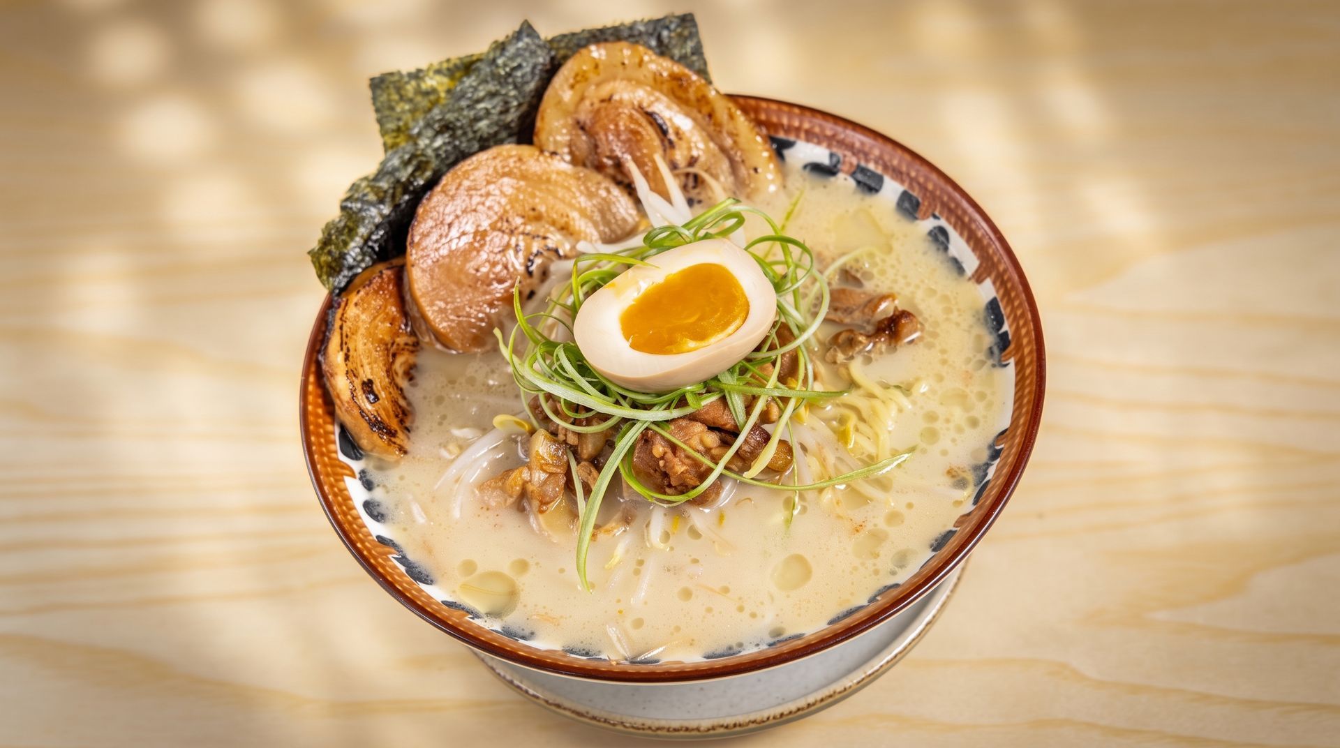 Bowl of ramen with soft-boiled egg, pork slices, seaweed, and scallions in creamy broth