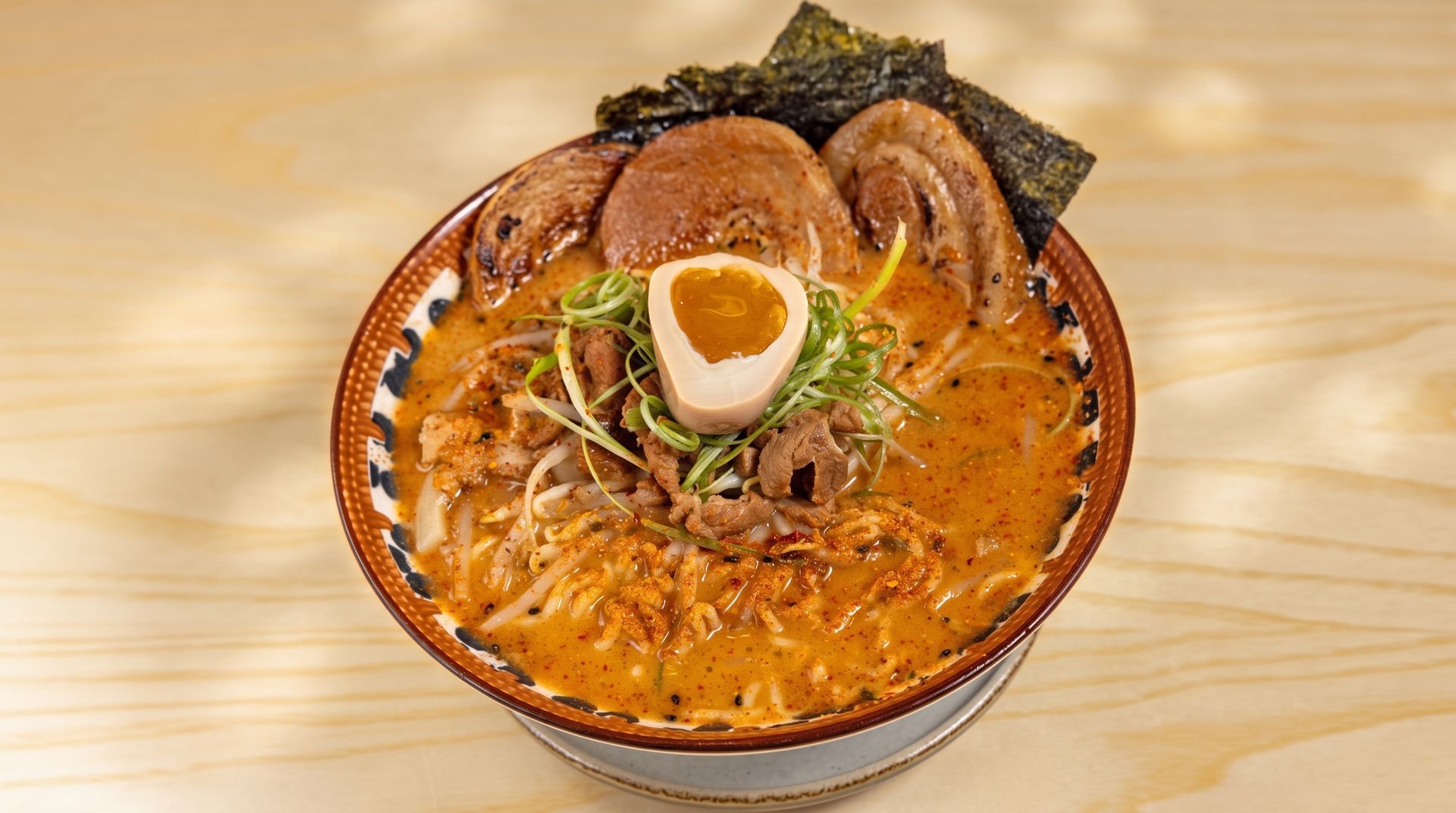 A bowl of ramen with broth, noodles, sliced pork, egg, and seaweed on a wooden table