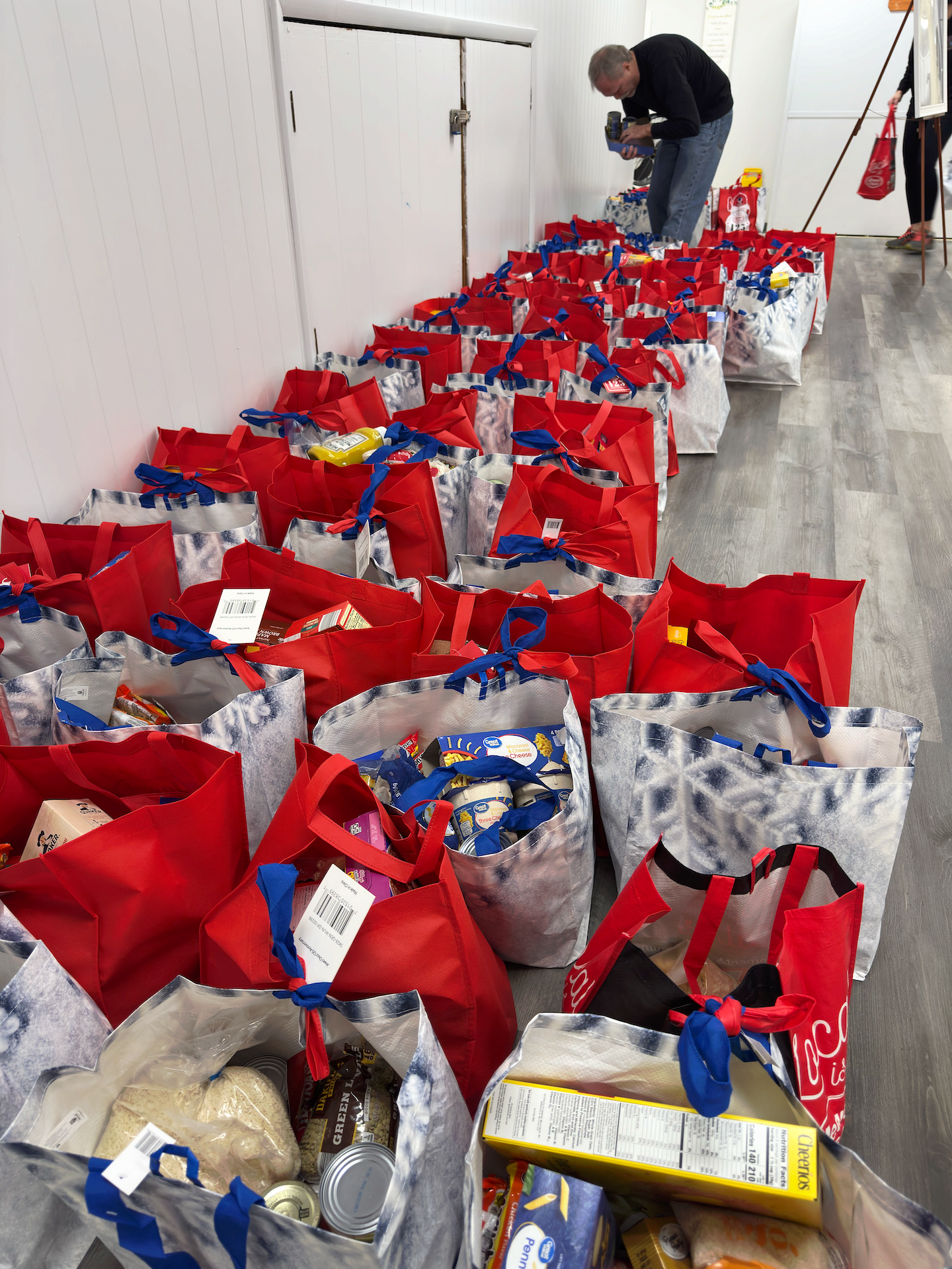 Rows of red gift bags lined up indoors, with a person sorting items in the background.