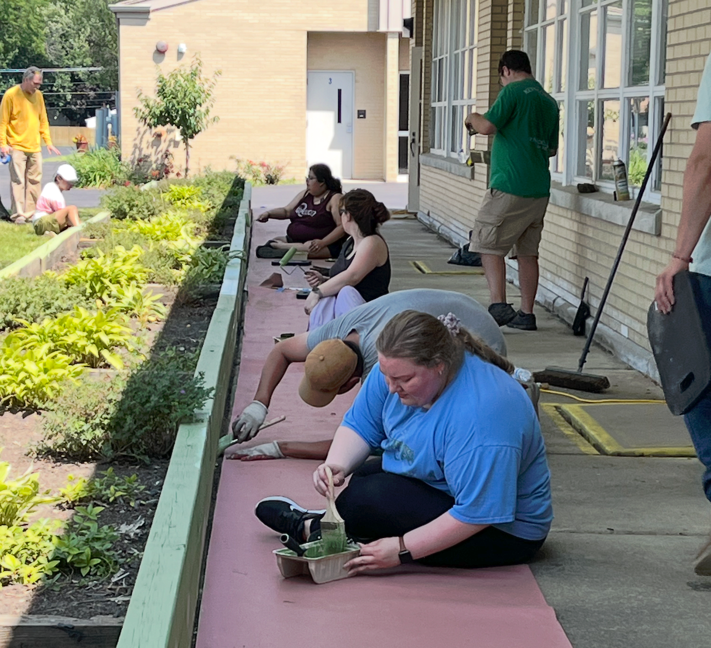 People seated on a school walkway, tying shoes and preparing for an outdoor activity.