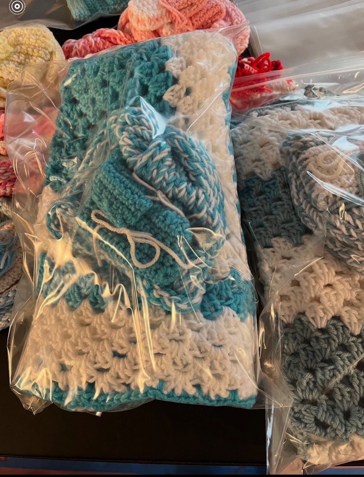 Plastic bags of blue and white crocheted fabric pieces on a table, with red and beige items nearby