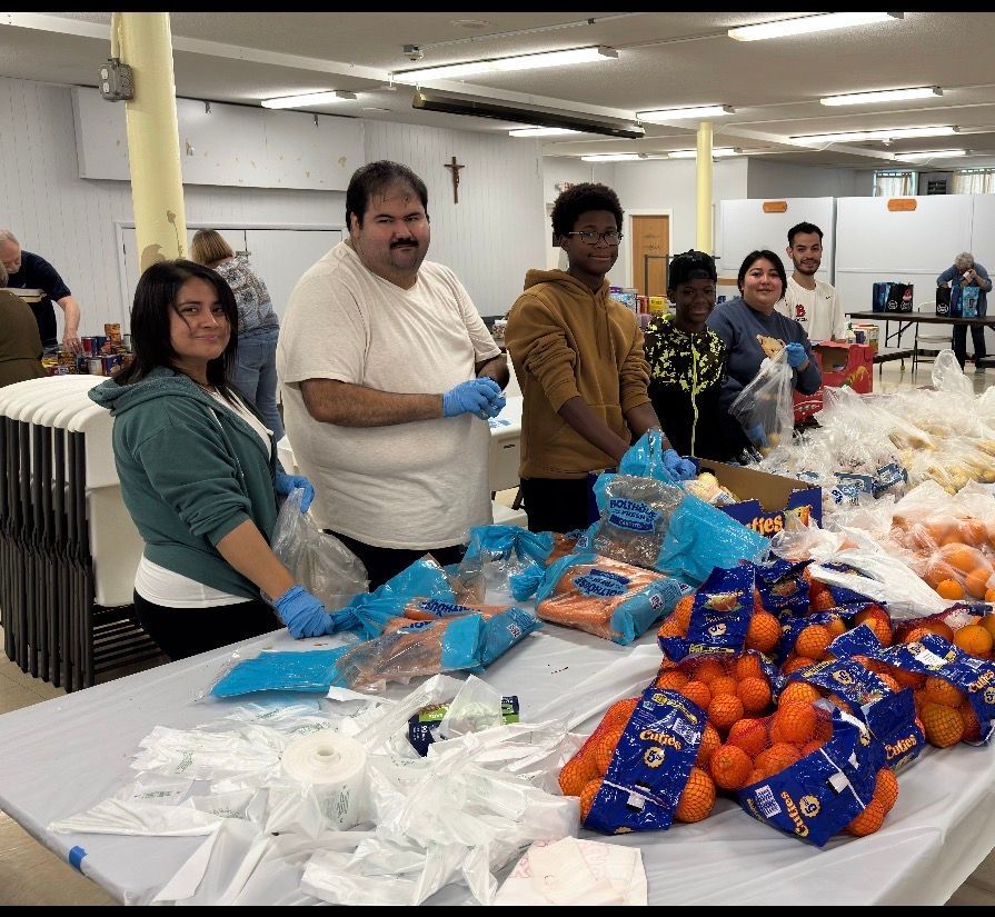Volunteers packing blue and orange care packages on a long table in a bright indoor hall