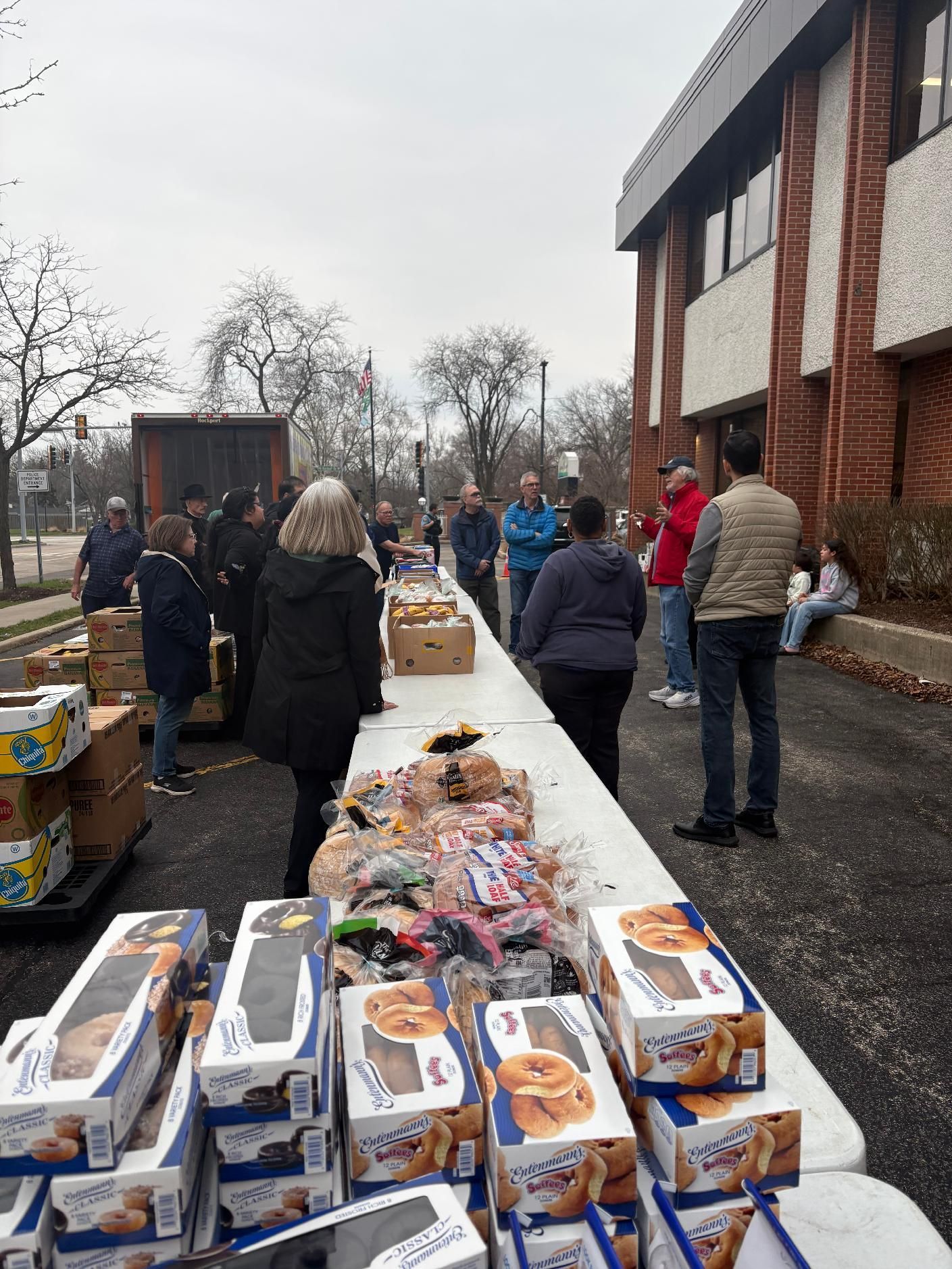 People browsing tables of donated goods outside a brick building on a cloudy day