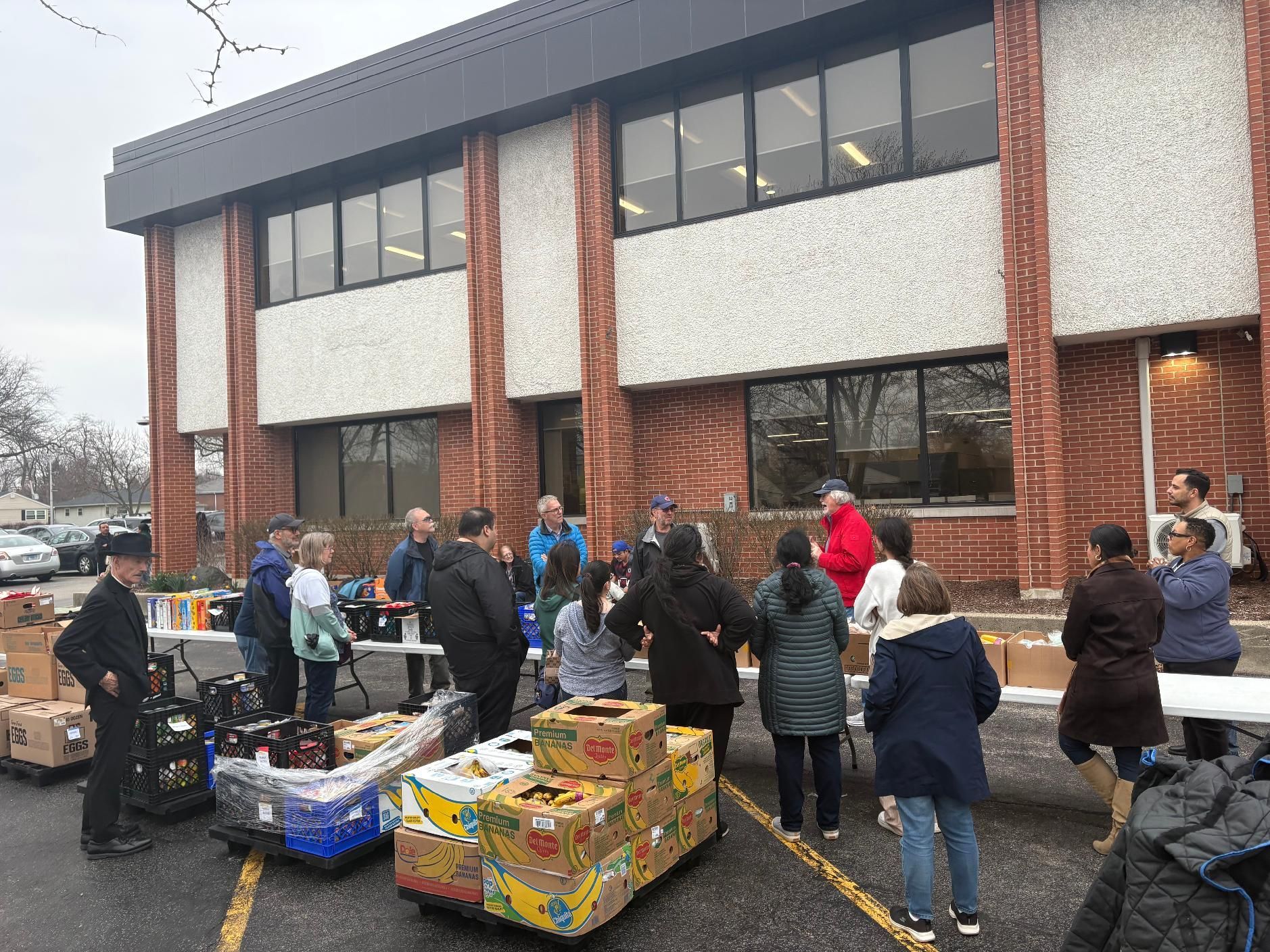 Volunteers sort donated food boxes outside a brick building on a rainy day