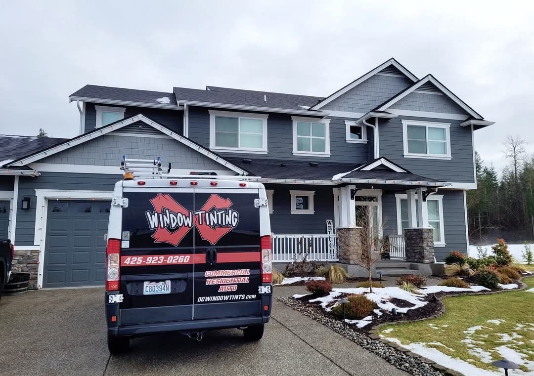 A dark van parked in a driveway in front of a gray two-story house with light snow on the ground.