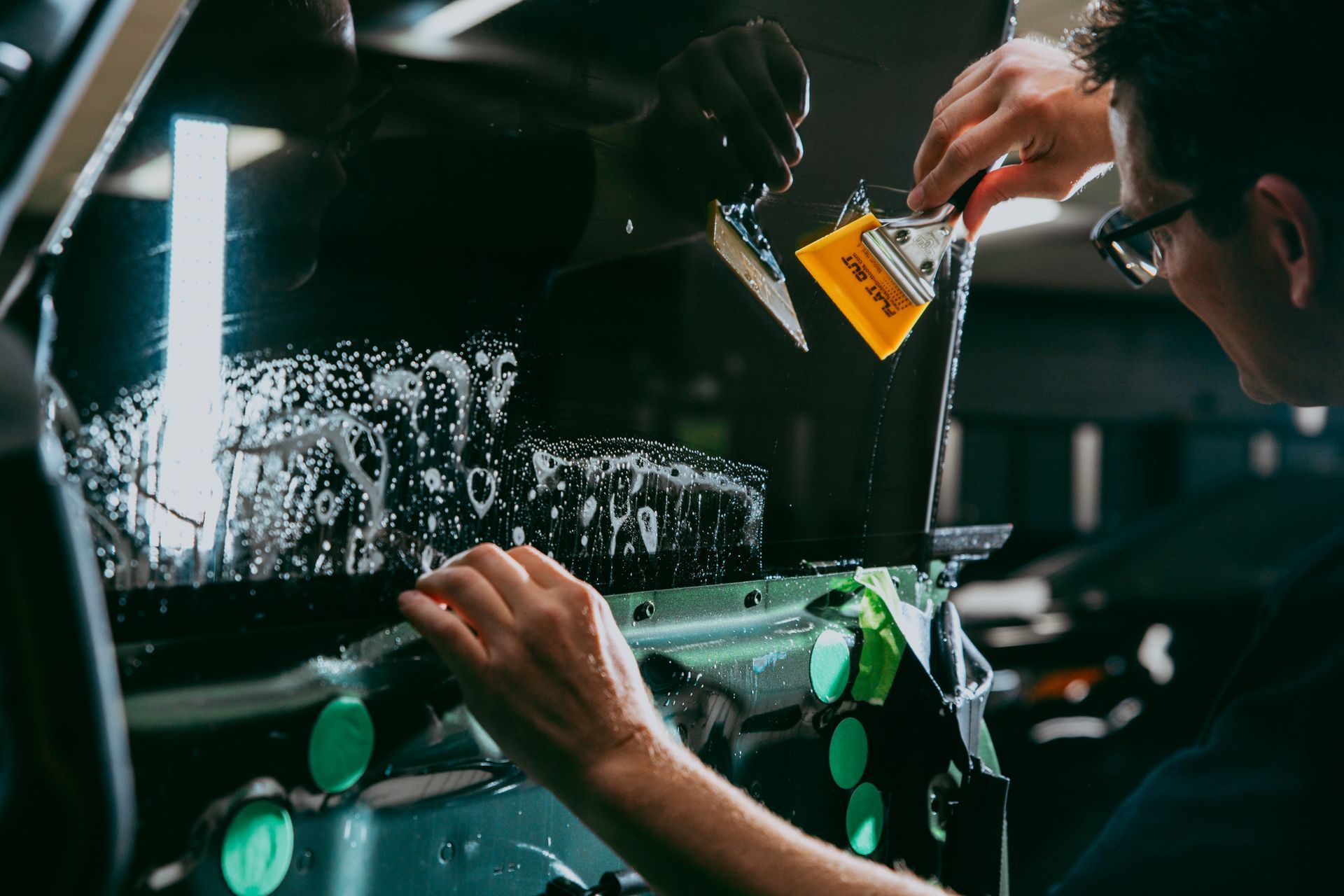 Person applying tint to a car window with a squeegee, in an auto shop.