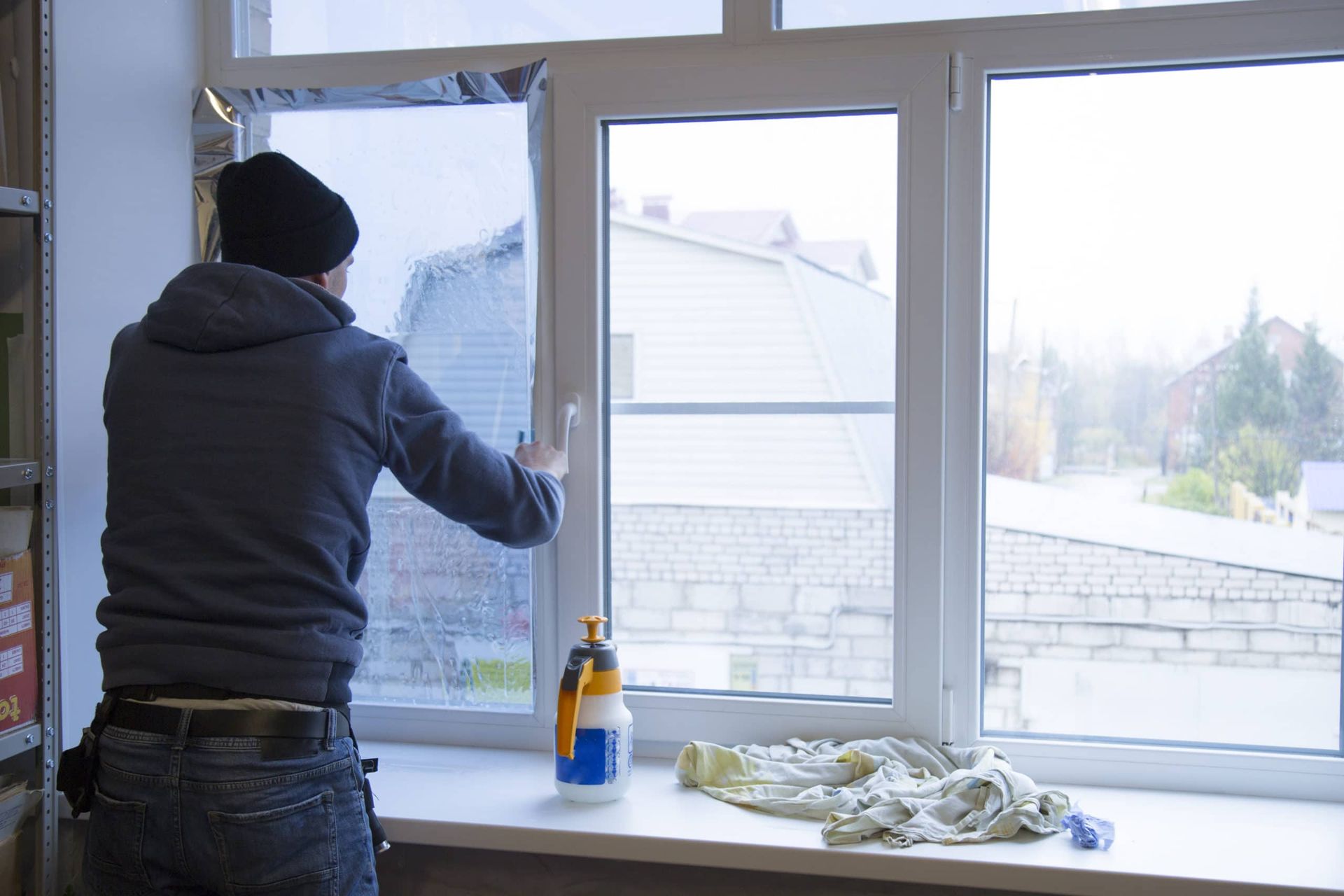 Person applying window tint to a multi-pane window, using a sprayer and squeegee.