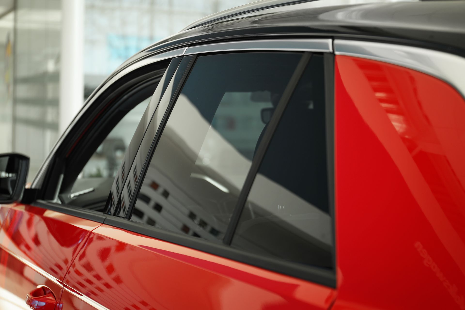 Red car's side with tinted windows, chrome trim, and black roof.