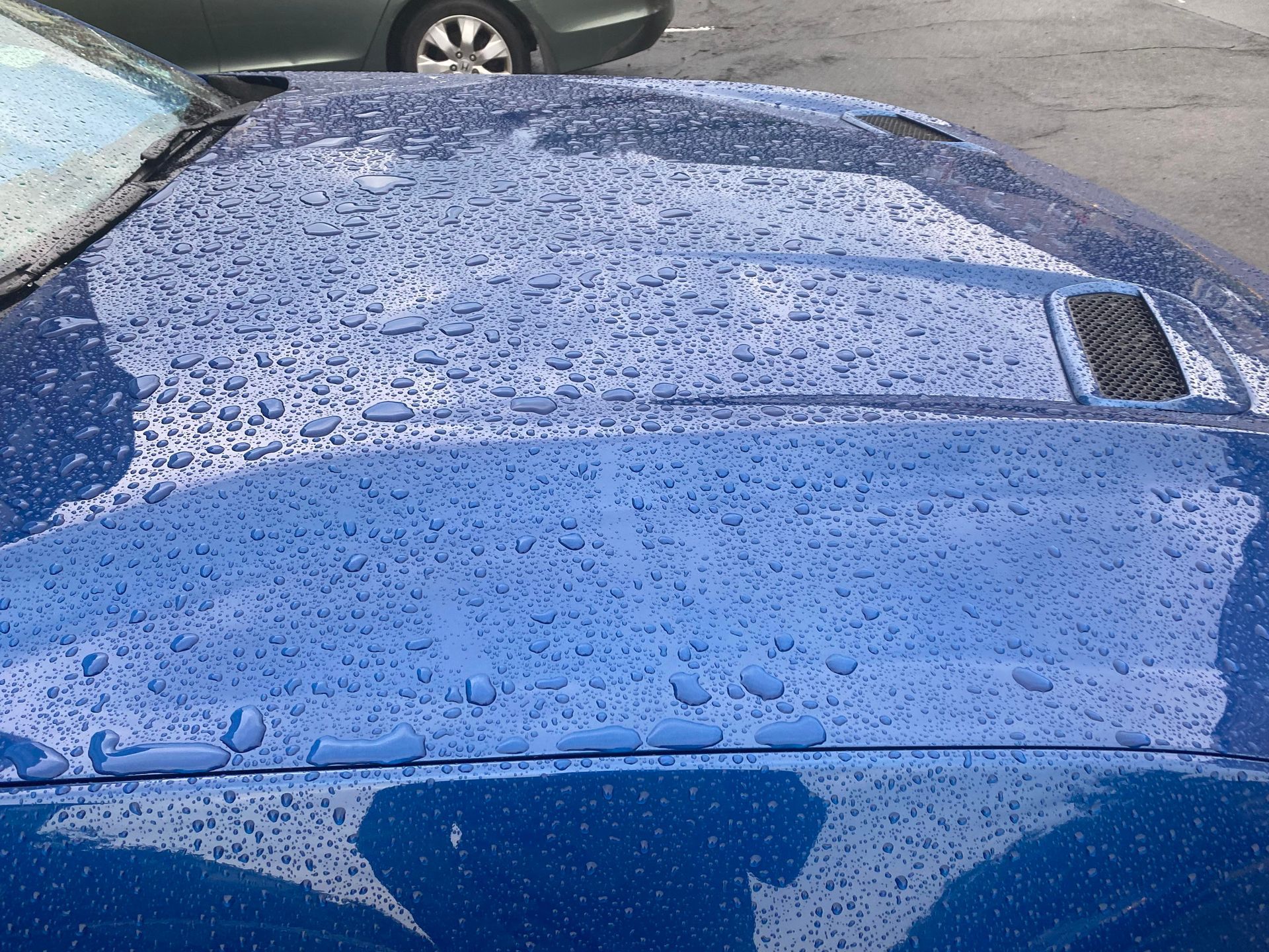 Blue car hood covered in raindrops.