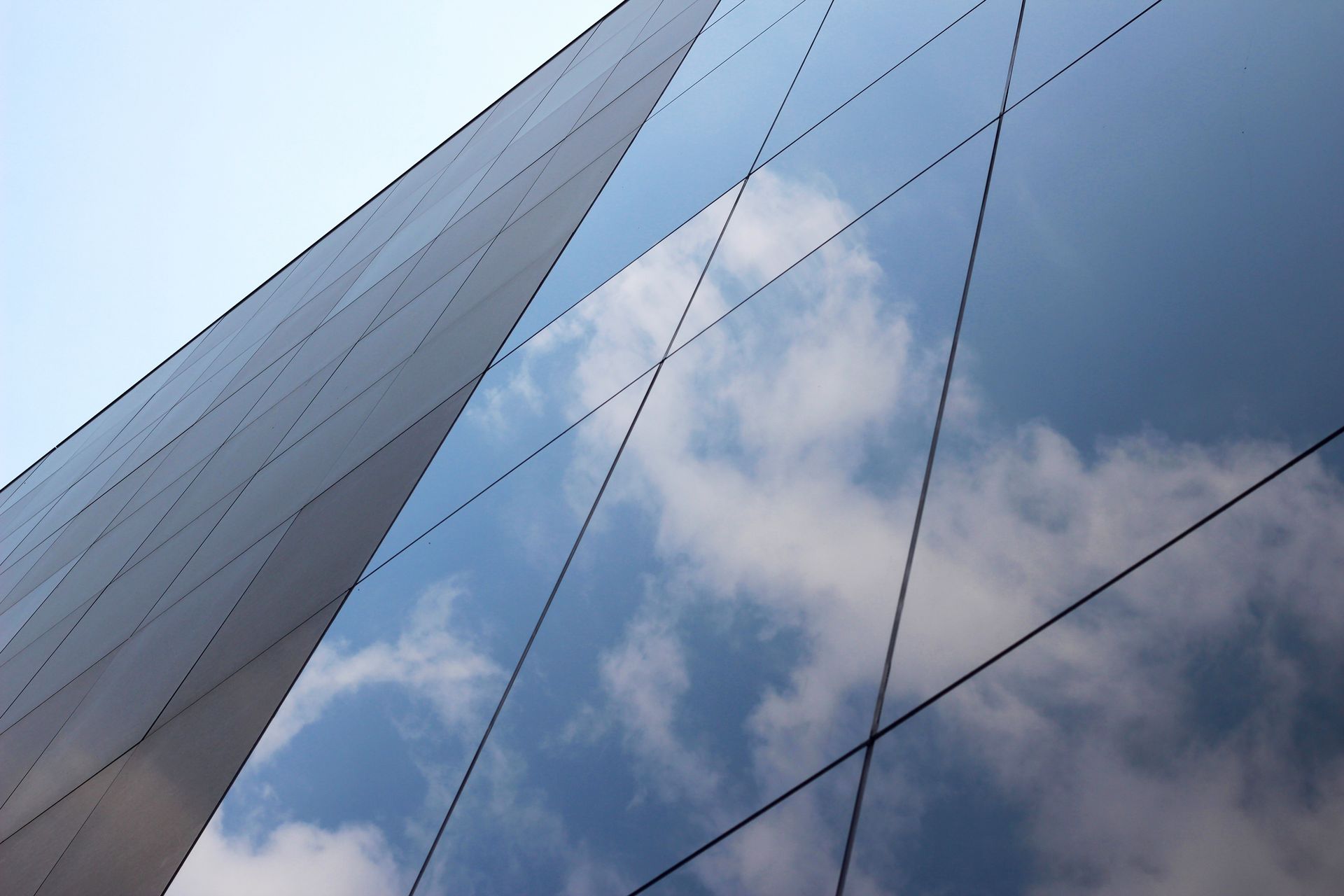 Glass facade of a building reflecting a blue sky with fluffy white clouds.