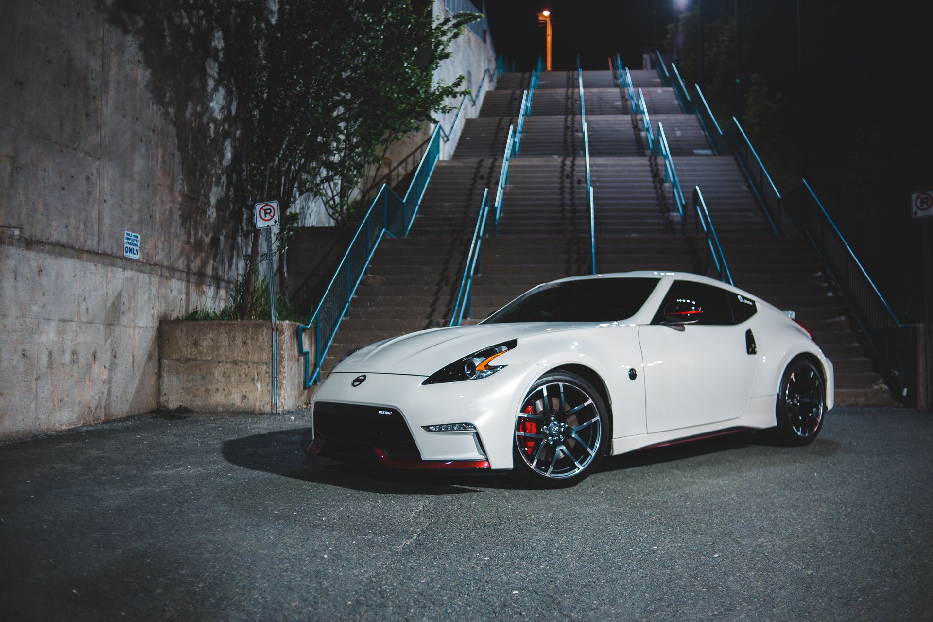 White Nissan 370Z sports car parked on a street at night, with stairs leading up to a lit street light.