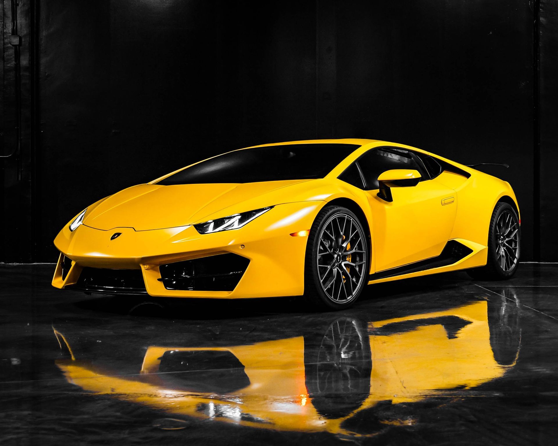 Yellow Lamborghini sports car, parked on a shiny black surface with a matching reflection.