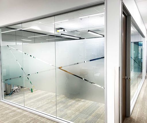 Office space with frosted glass walls and geometric designs. A door is visible.