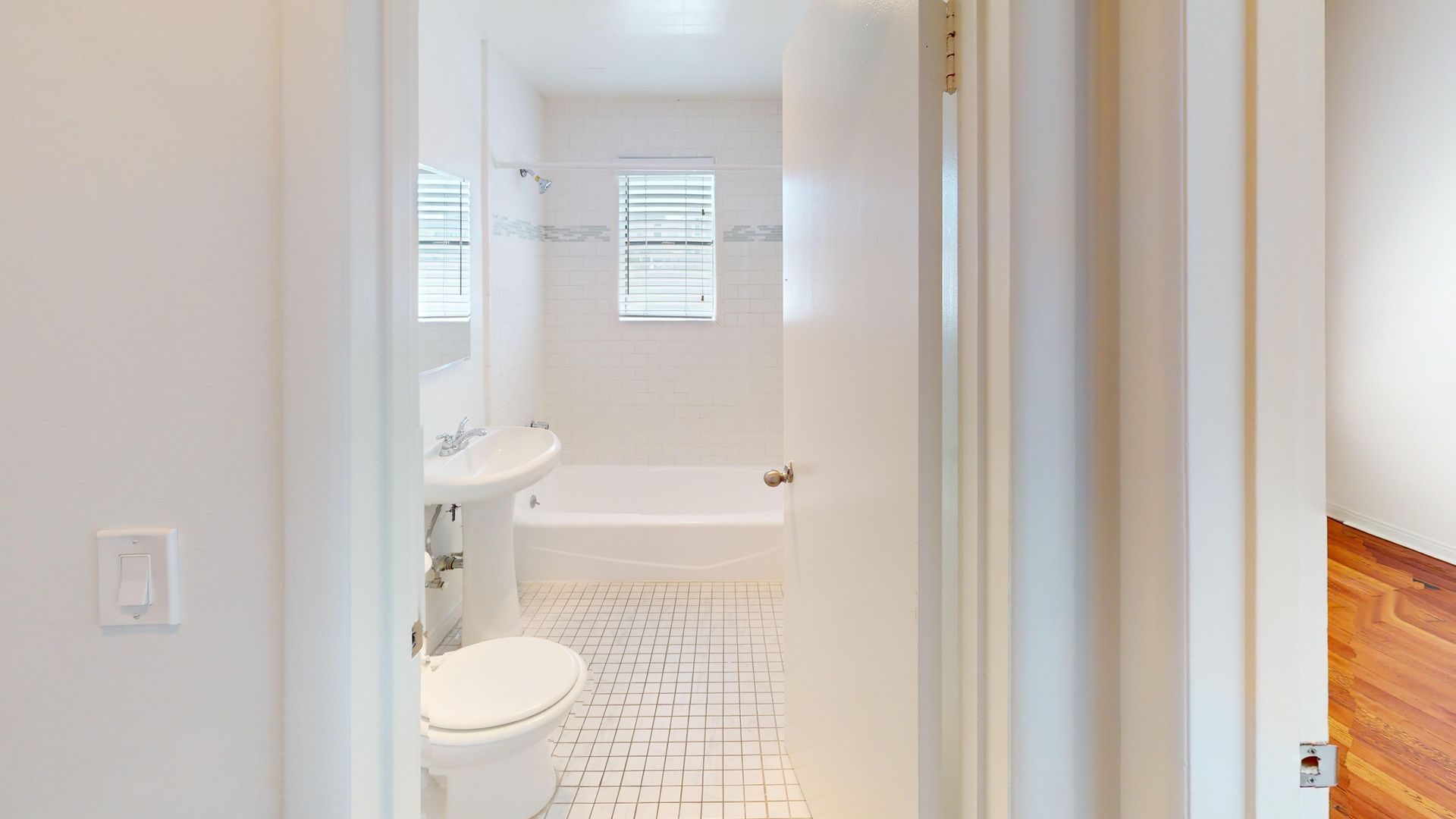 Bathroom interior with white walls, a sink, toilet, and bathtub visible through the doorway.