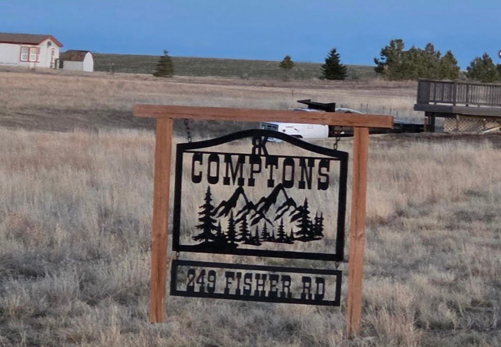 Comptons sign in a grassy field with mountains in the background, on Fisher Rd.