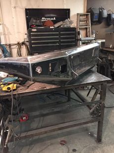 Large black metal boat hull on a workbench in a workshop, with tools and cabinets in the background