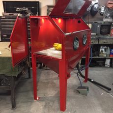 Red metal blasting cabinet with open doors and built-in gloves in a workshop garage