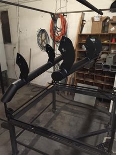 Black metal fabrication frame with pipes in a workshop, surrounded by coiled cables and storage bins.