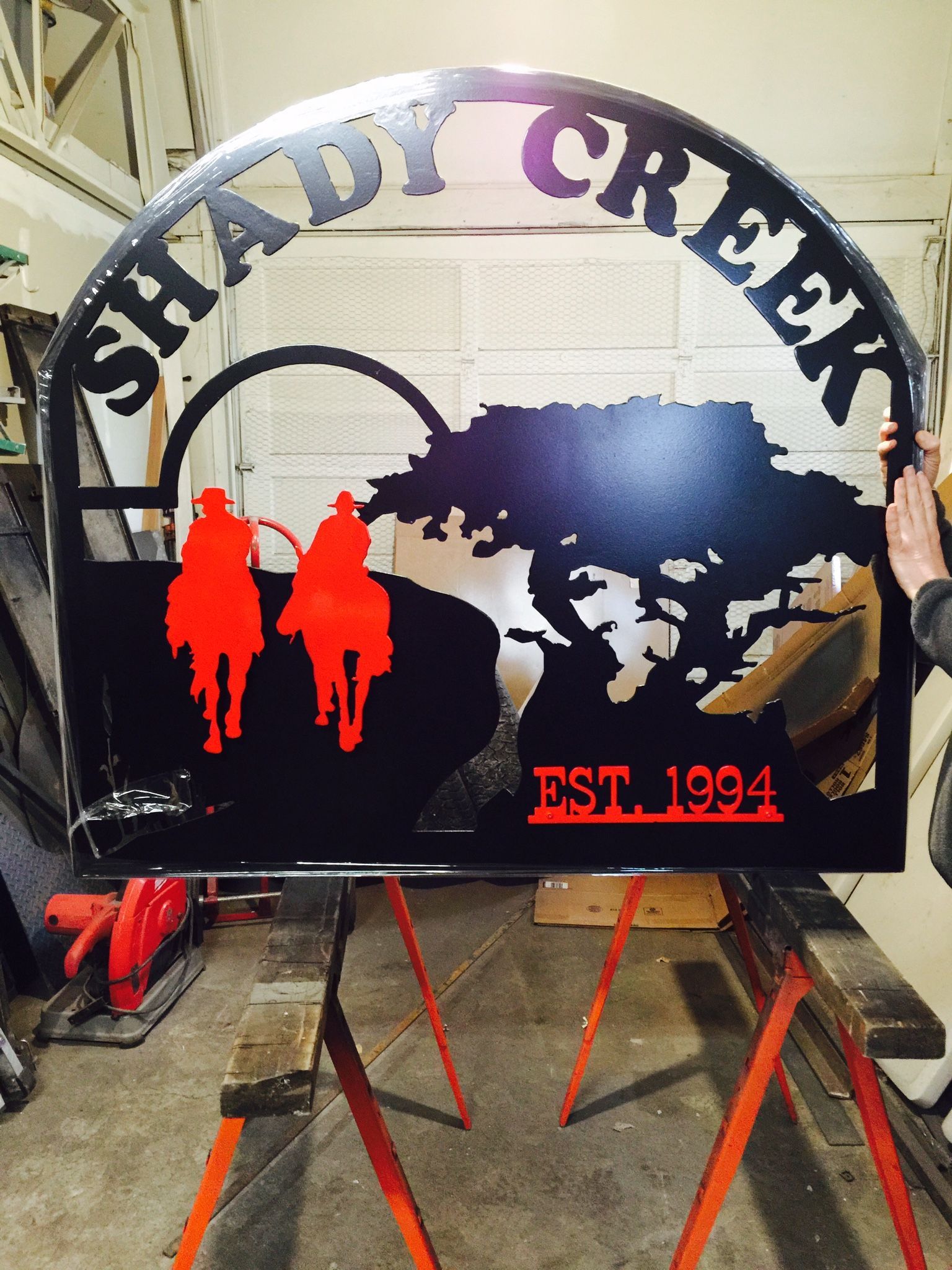 Shady Creek sign on easel, with dark map silhouette, red hiker figures, and “EST. 1994” text.