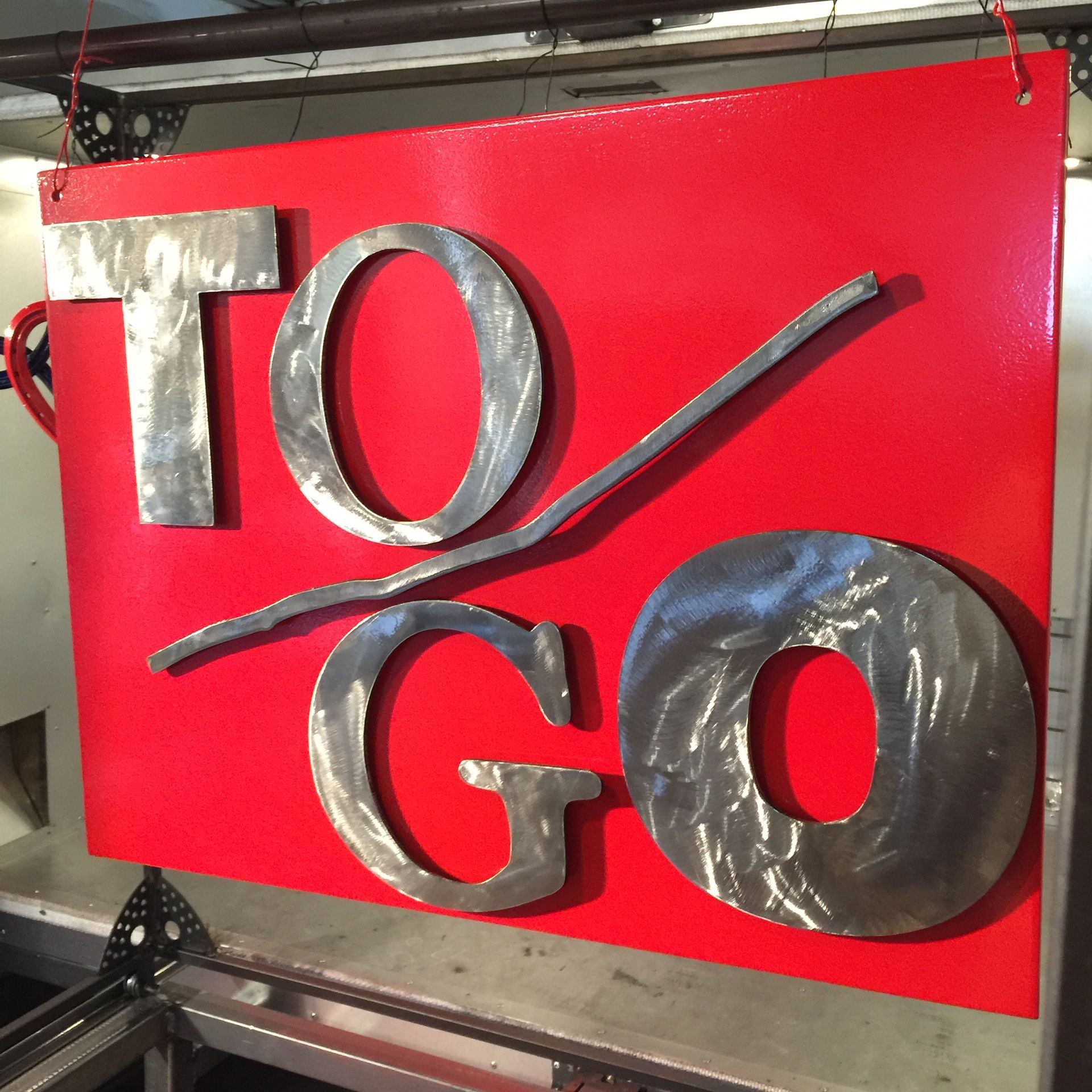 Red sign reading “TO/GO” in metallic letters on a bright red background.
