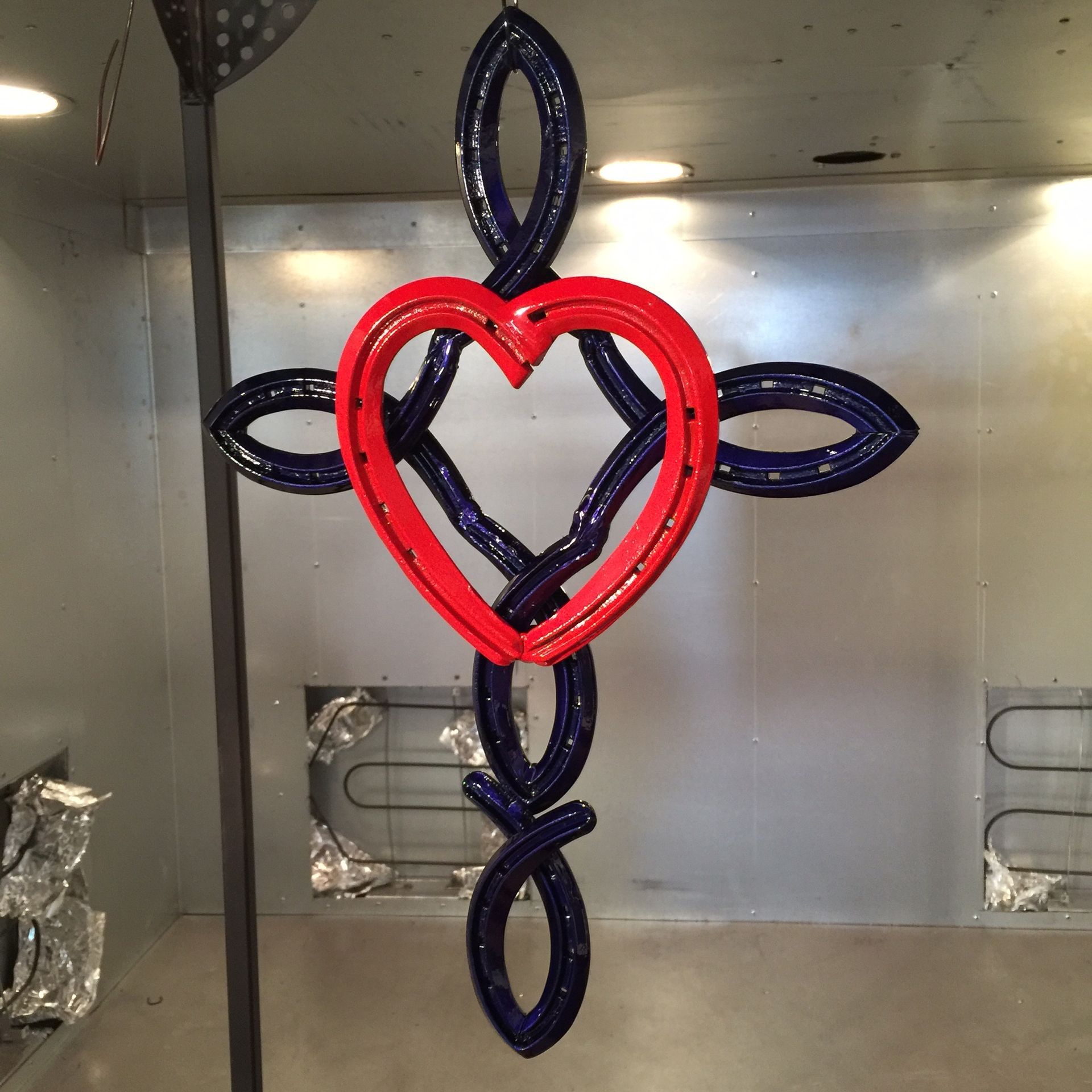 Red and navy balloon heart with four navy petal-like loops, hanging against a metallic wall.