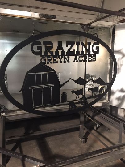 Black metal sign on a machine reads “GRAZING GREEN ACRES,” with a barn and farm scene cutout.