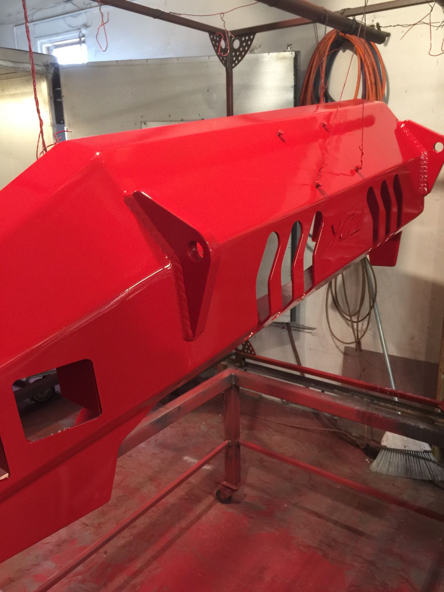 Red industrial machine part suspended in a workshop, with cables and metal framing visible.