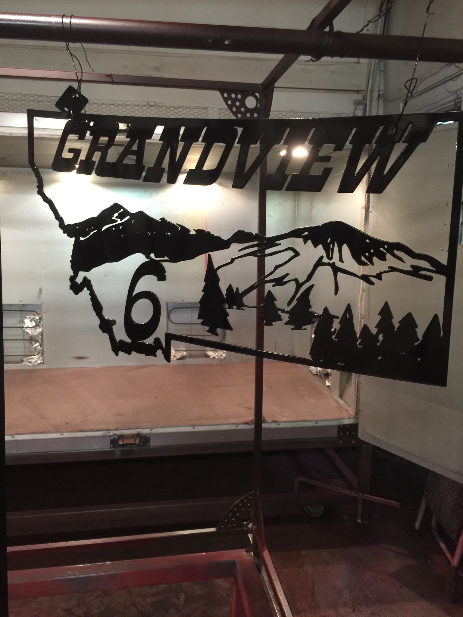 Black metal wall art with mountains, trees, and a large “6,” hanging indoors.