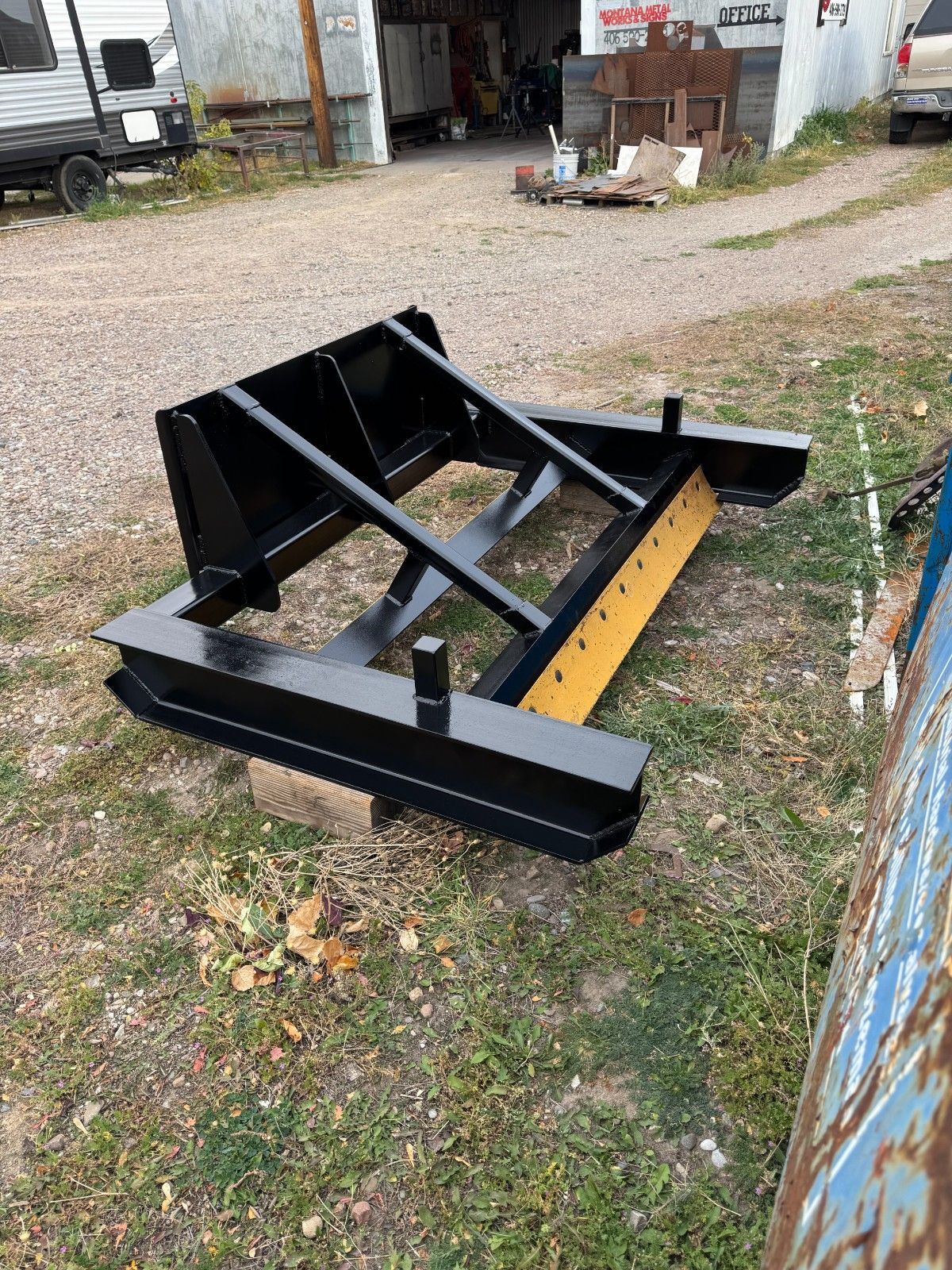 Black metal snow plow attachment on gravel in an outdoor yard near a building.