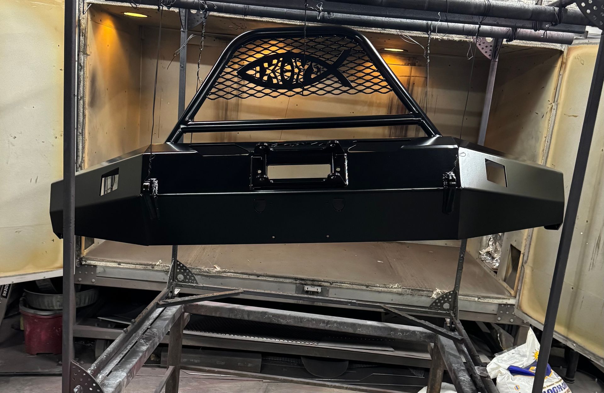 Black metal vehicle body or frame in a workshop, mounted on a stand with shelves and tools nearby
