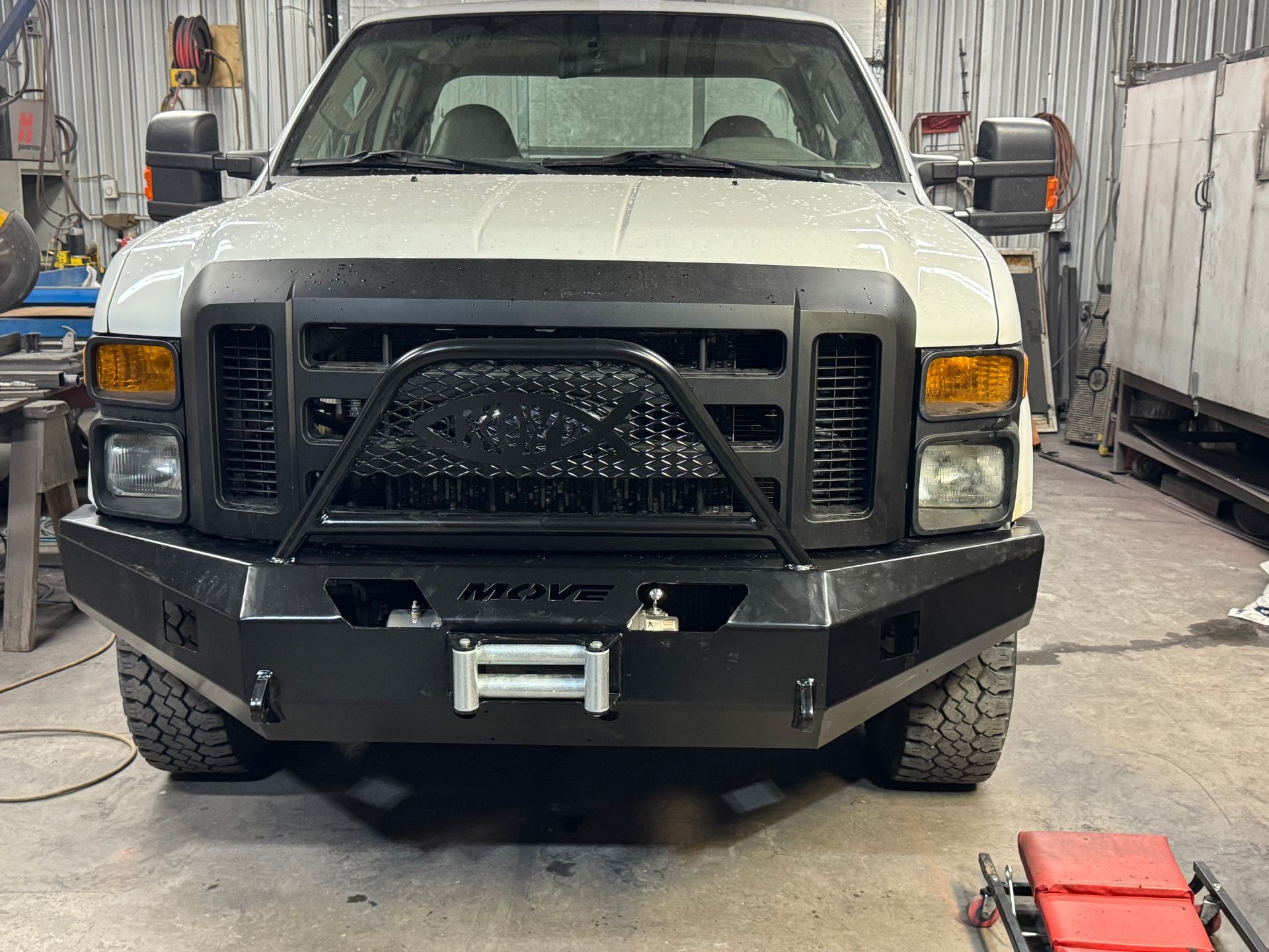 Front view of a white pickup truck in a garage, with a black grille guard and winch bumper.