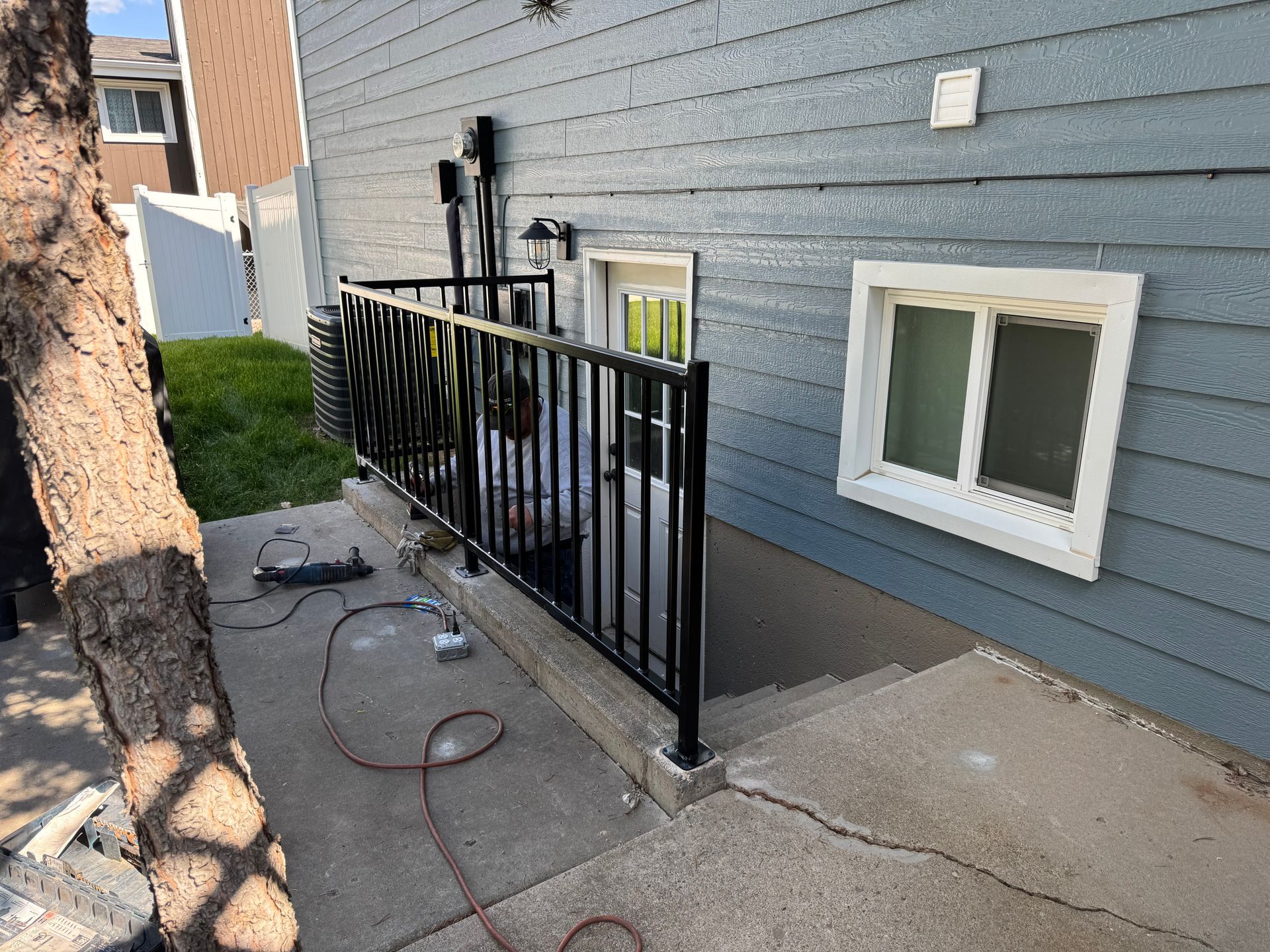 Black metal railing beside a gray house along a concrete path with a hose and small window