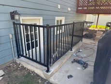 Black metal railing around a small concrete patio beside a blue house, with tools on the ground.