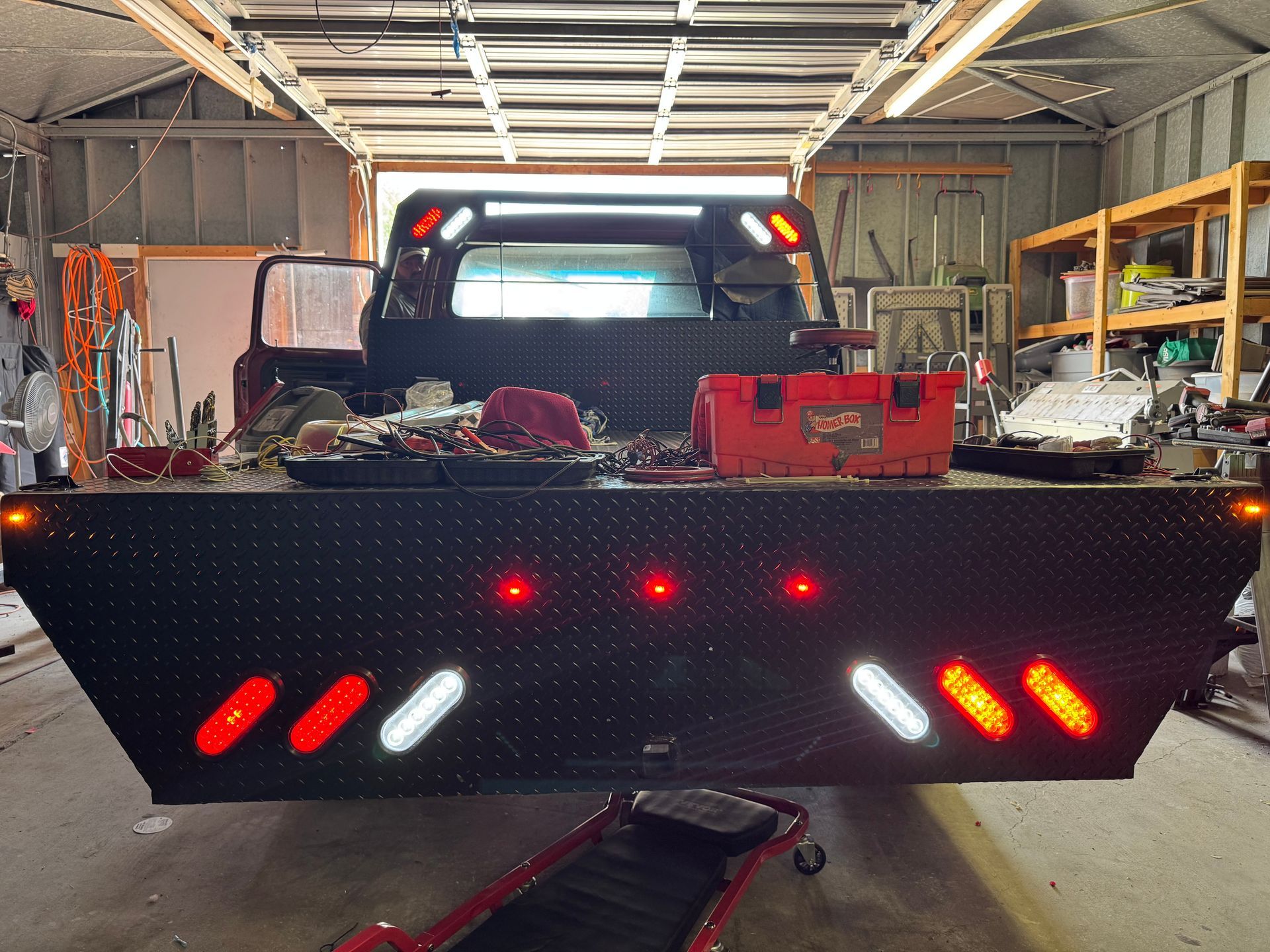 Red pickup truck with a black snowplow blade in a garage, rear lights glowing red and white.
