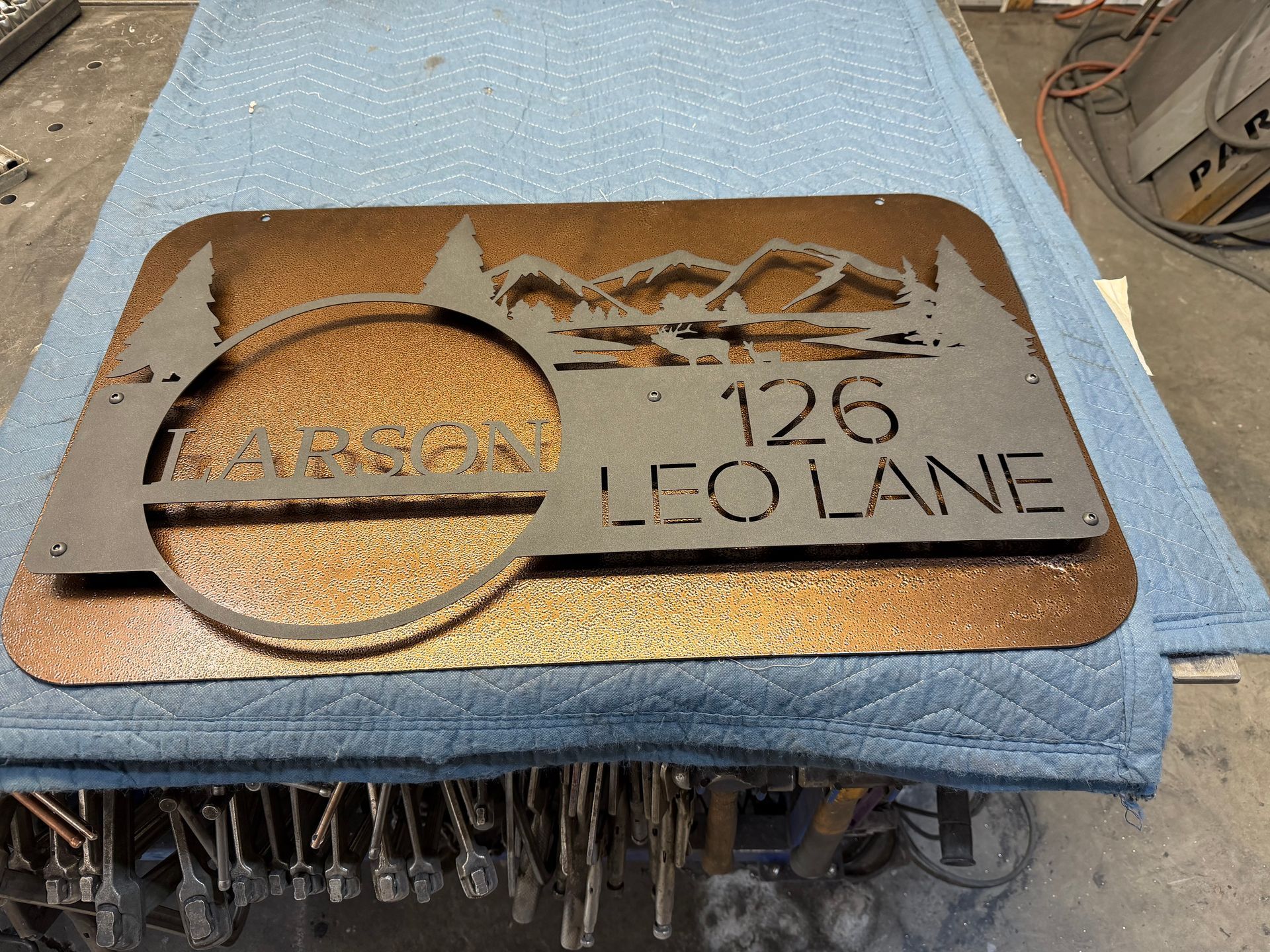 Rusty metal address plaque reading “126 LEO LANE” on blue fabric workbench