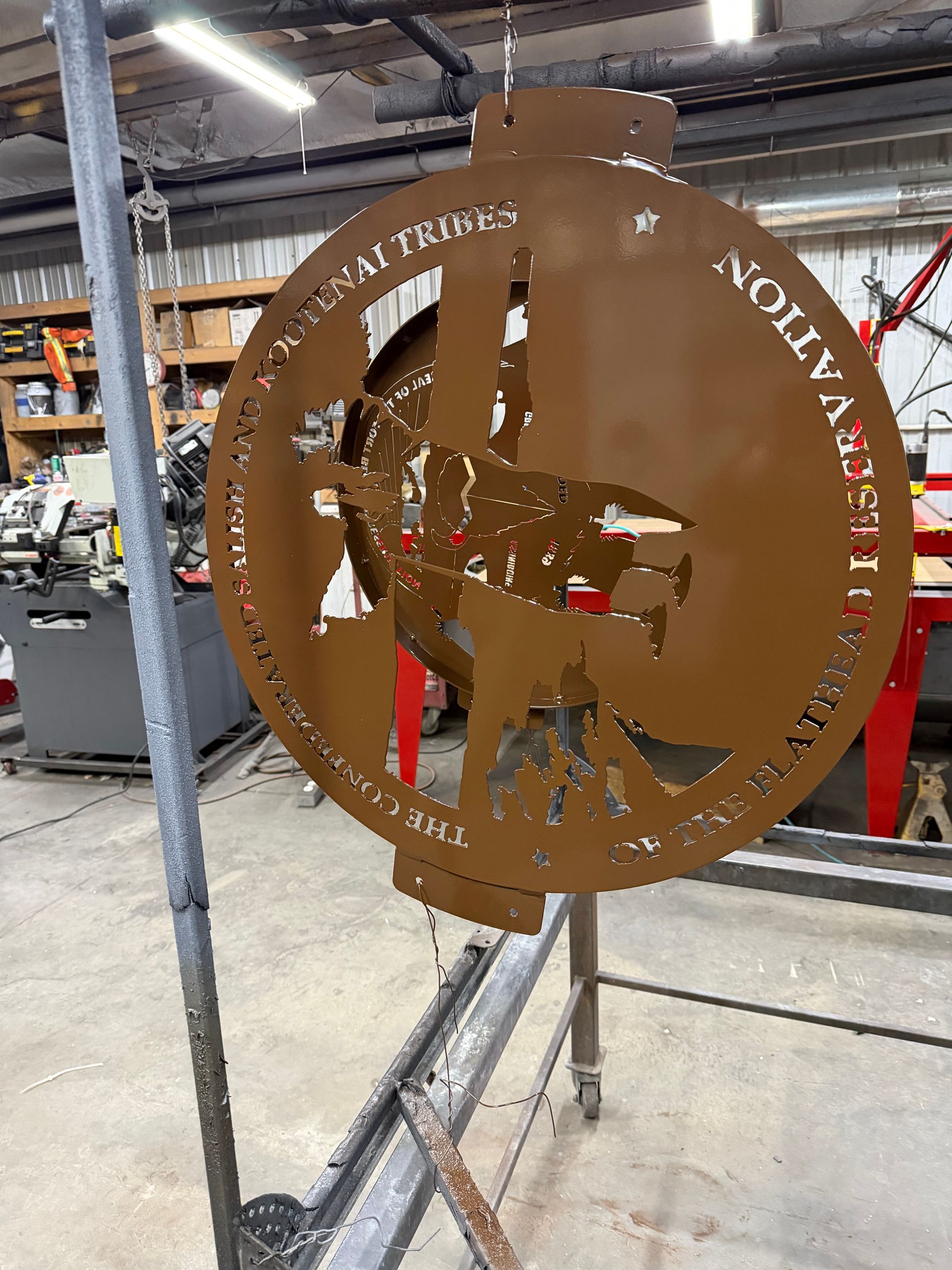 Rusty metal circular sign with cutout logo, standing in an industrial workshop or warehouse.