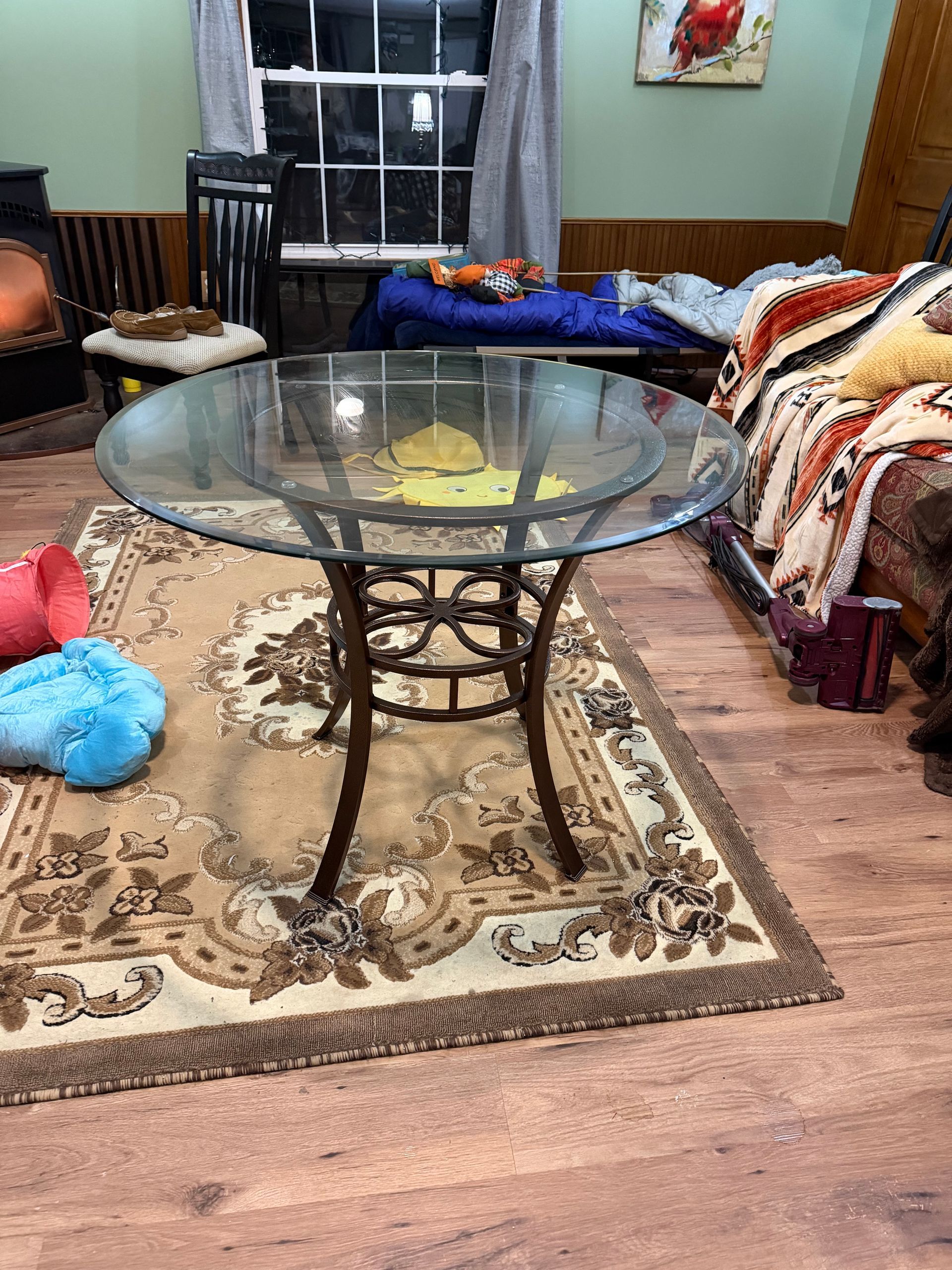 Living room with glass coffee table on patterned rug, couch, toys, and a window in the back.
