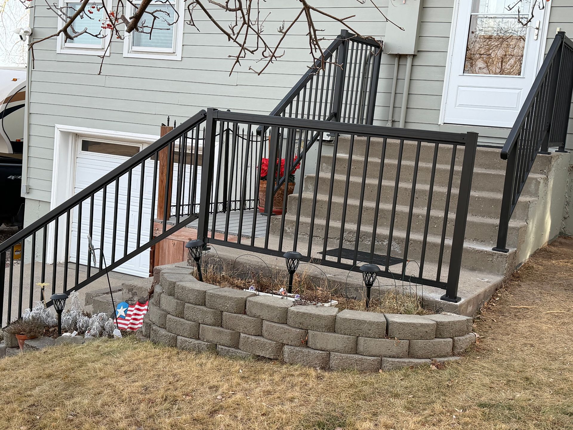 Front steps with black metal railings and red flower pots at a gray house entrance