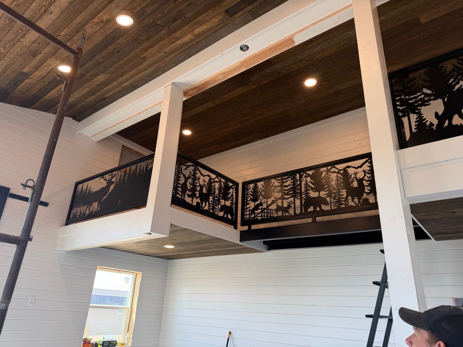 Interior of a modern loft with white beams, black balcony railings, and a wood ceiling