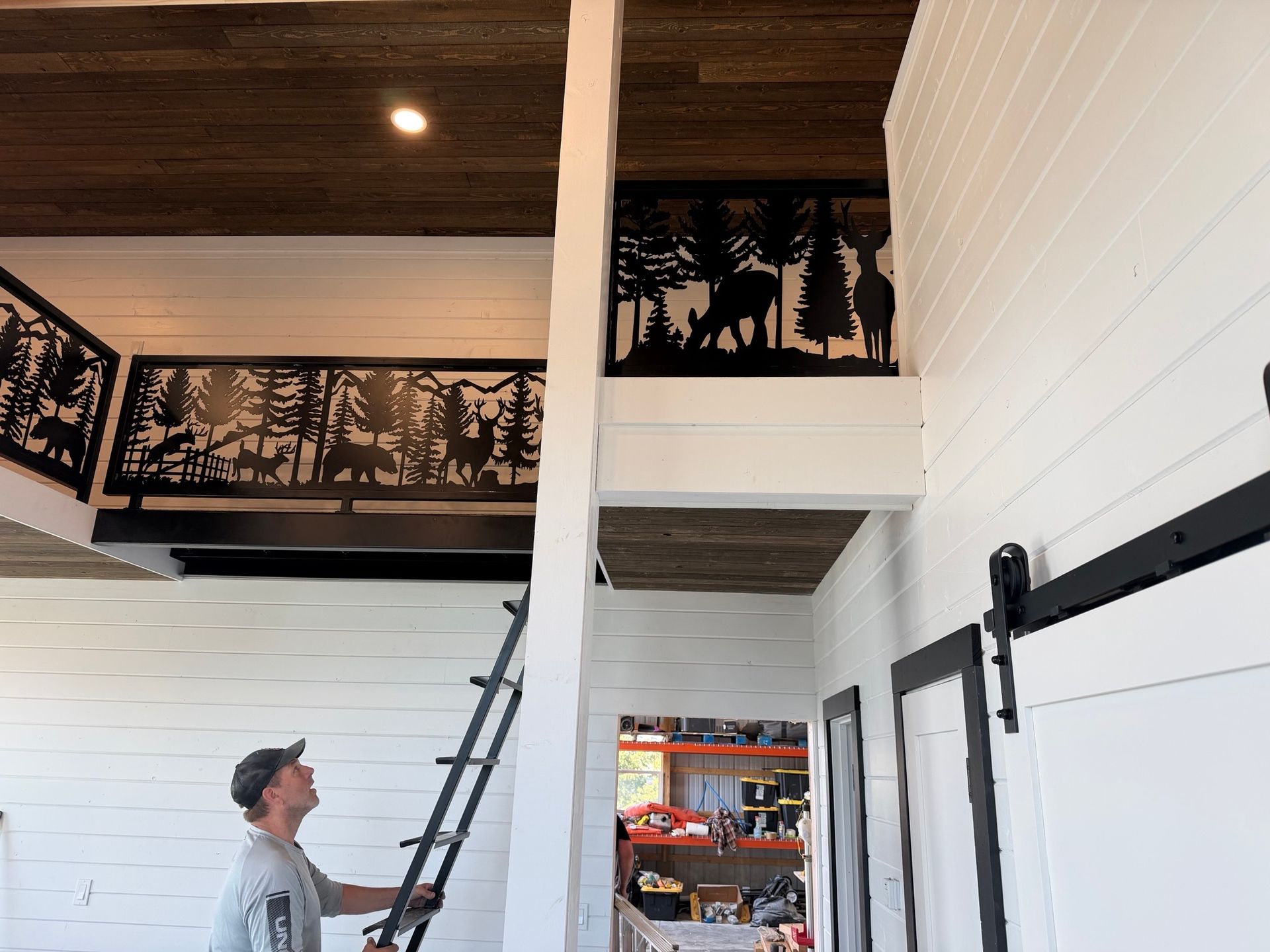 Person on a ladder in a white room with a loft and black railing art panels