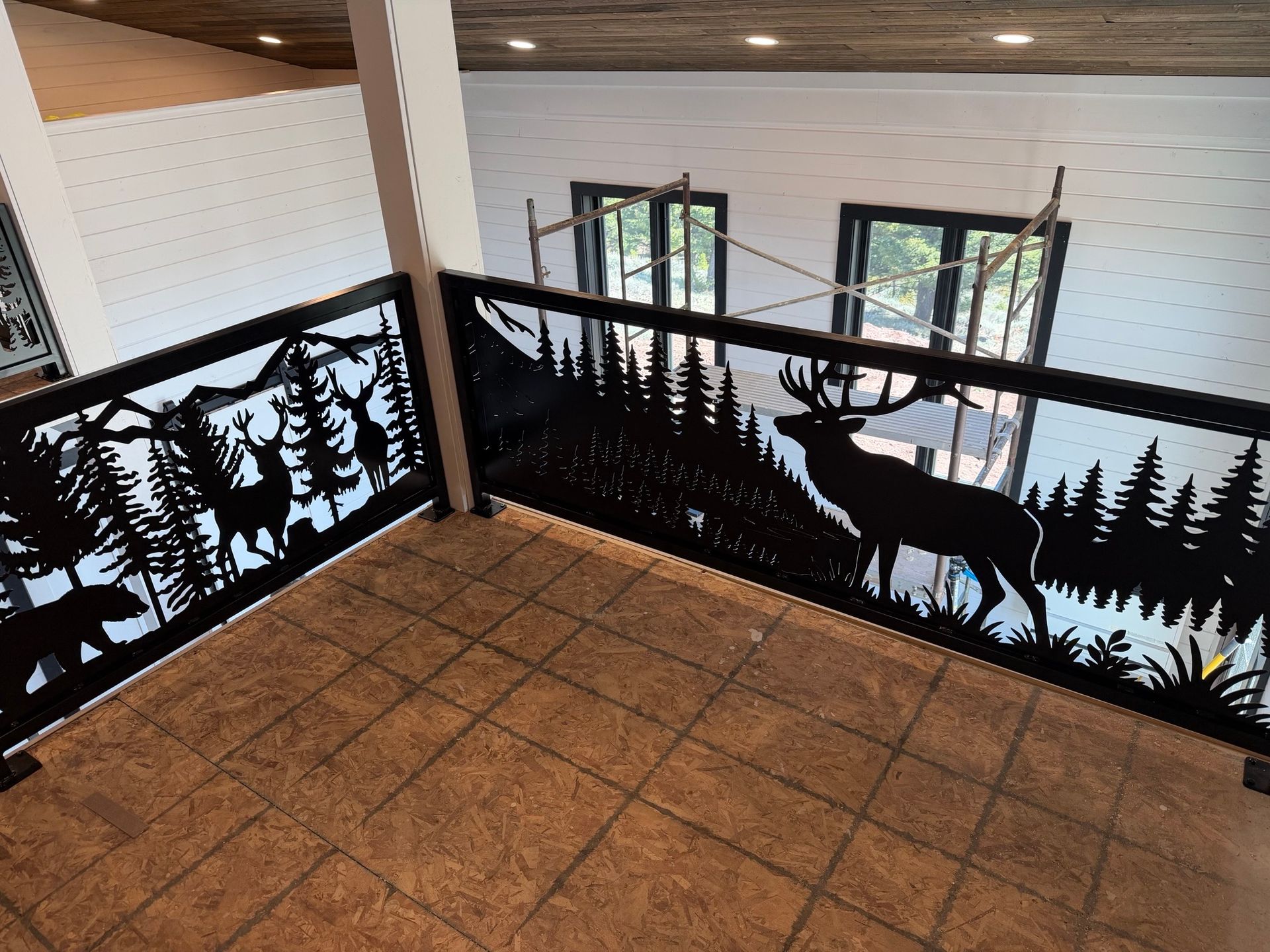 Indoor balcony with black metal forest-and-deer railing overlooking a room with windows below