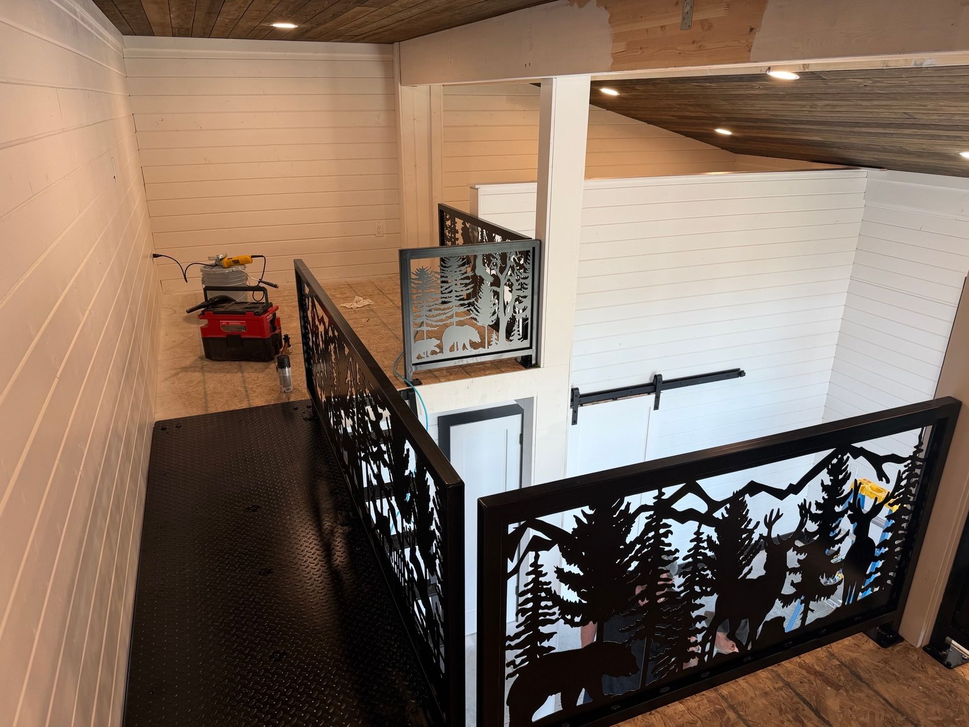 Indoor balcony walkway with black railings, white walls, and a red cart below the stairs